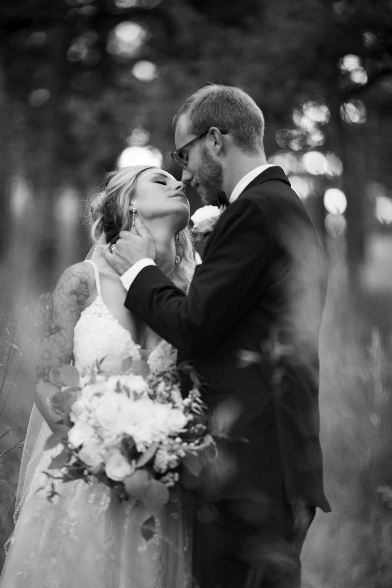 A romantic black and white wedding portrait of a couple embracing in a wooded setting.