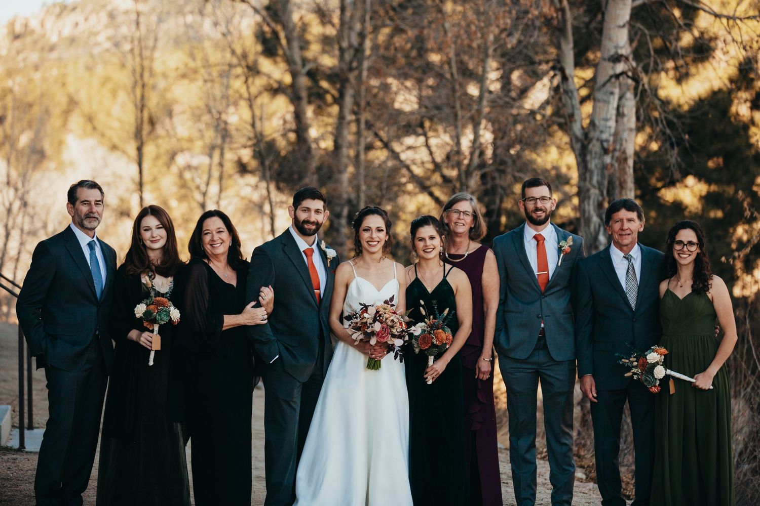 Formal wedding party portrait with navy suits and dark bridesmaid dresses against fall scenery.
