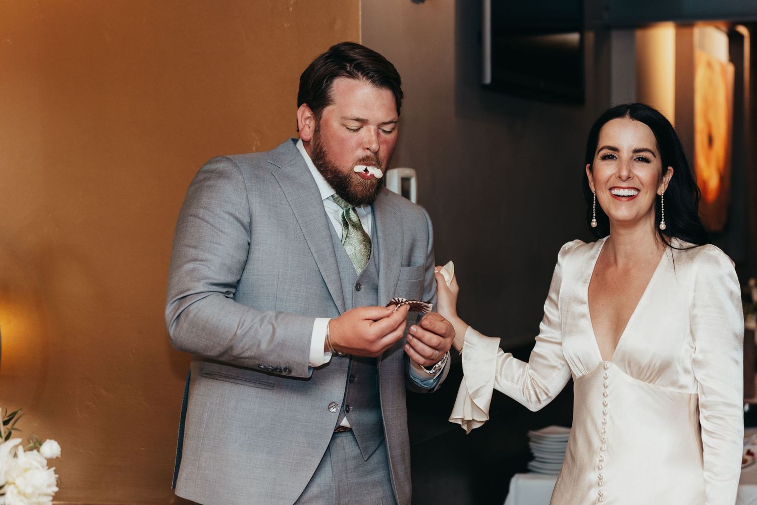 Wedding couple sharing cake during indoor reception celebration.