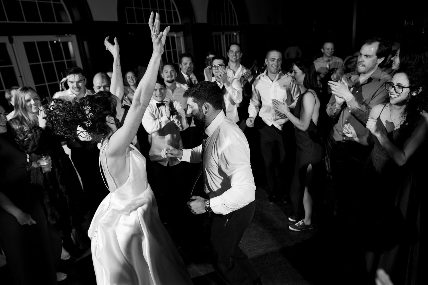 Black and white photo of wedding guests dancing and celebrating on a crowded dance floor.