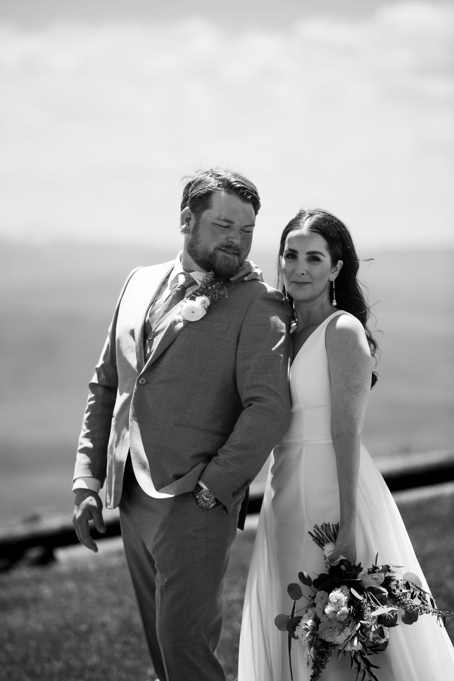 Black and white portrait of couple in wedding attire against mountain backdrop.