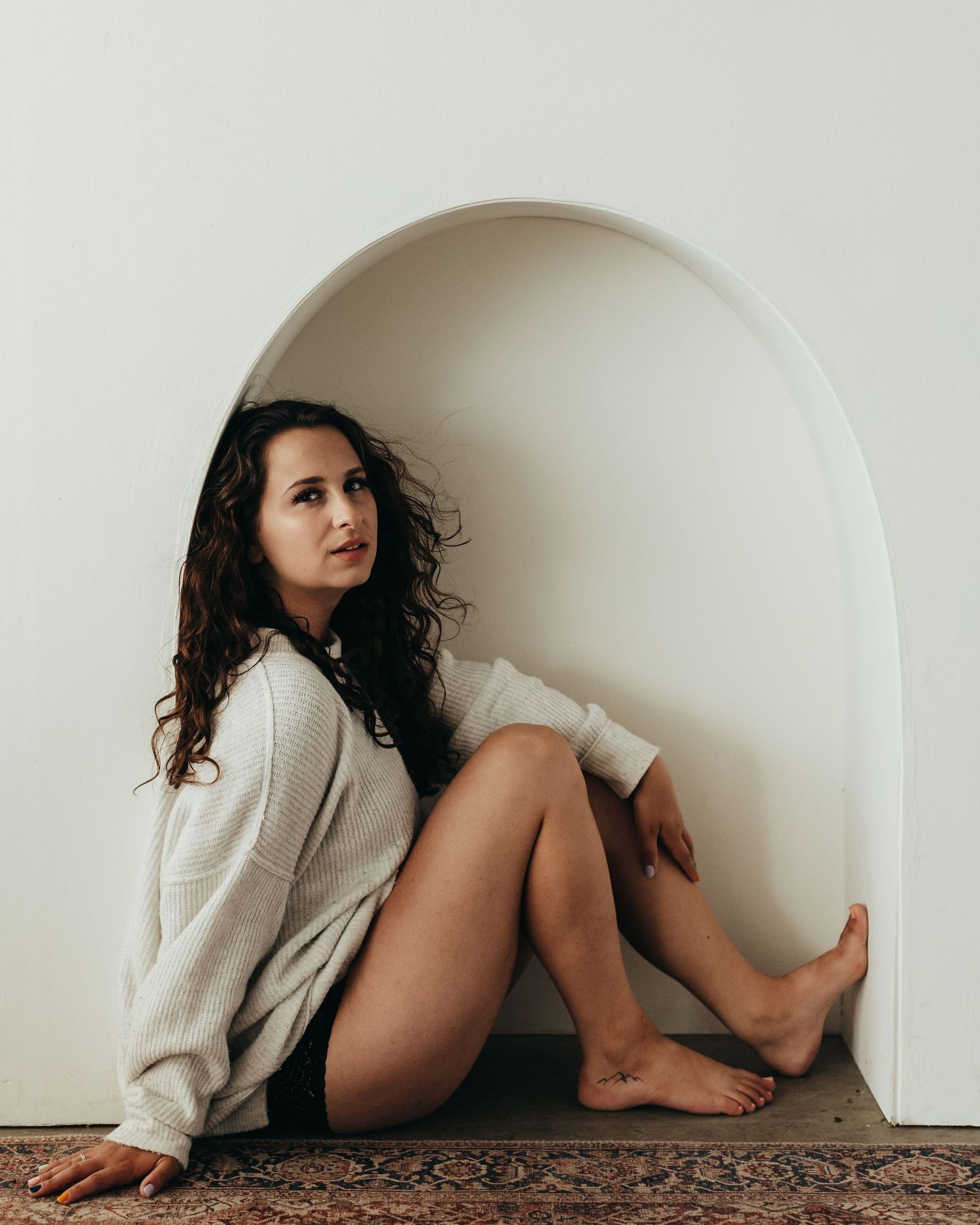 Woman in white sweater posing casually in a white arched alcove.