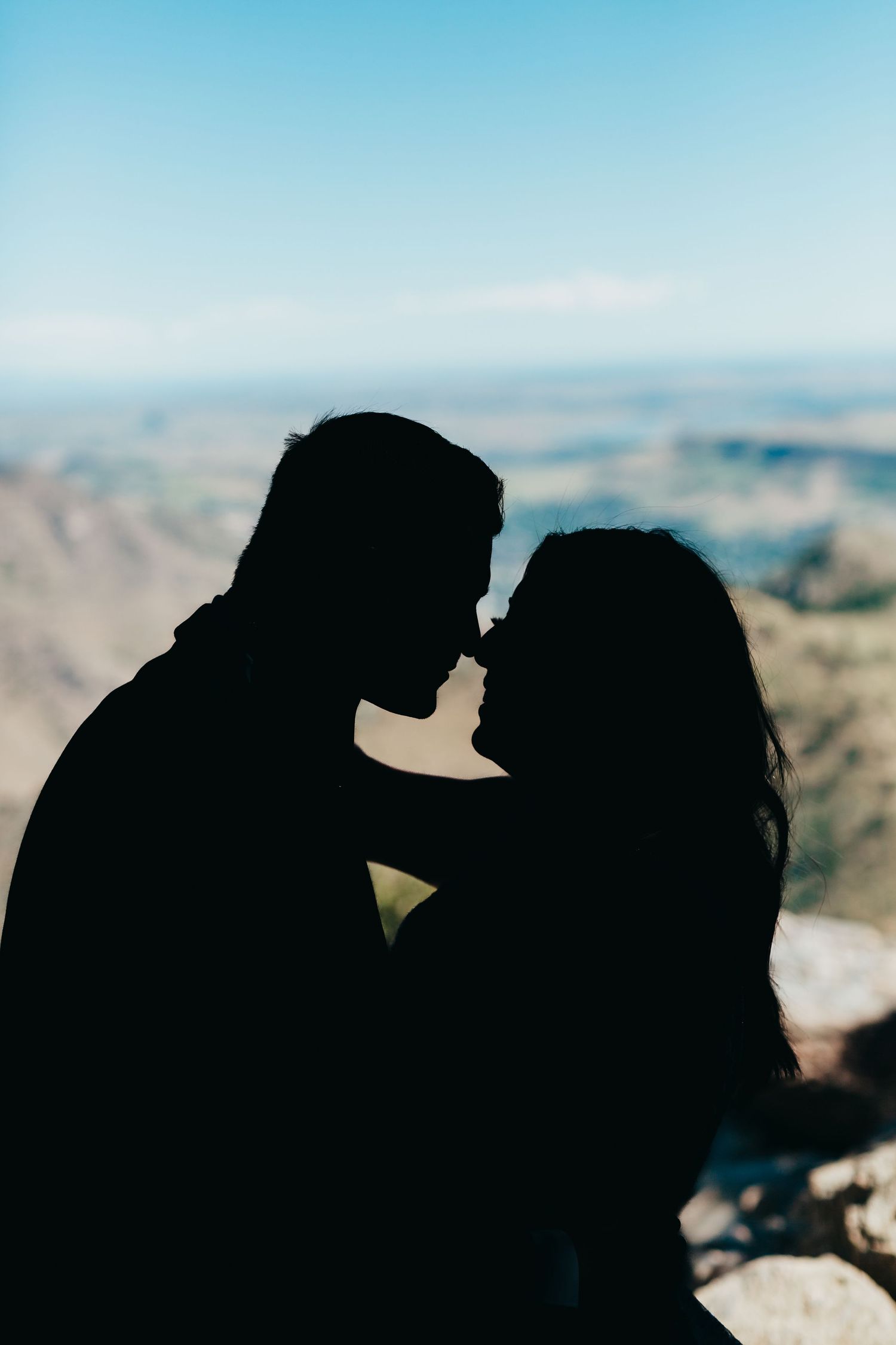 Silhouette of a couple about to kiss with mountain landscape in the background.