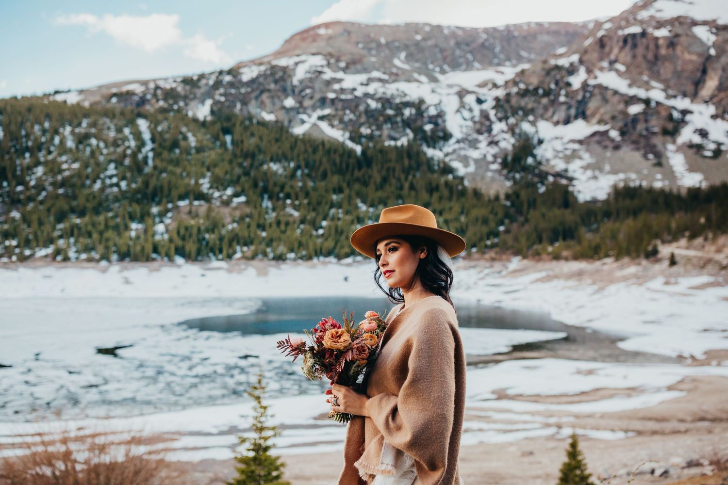 Person in brown coat holds bouquet against snowy mountain landscape.