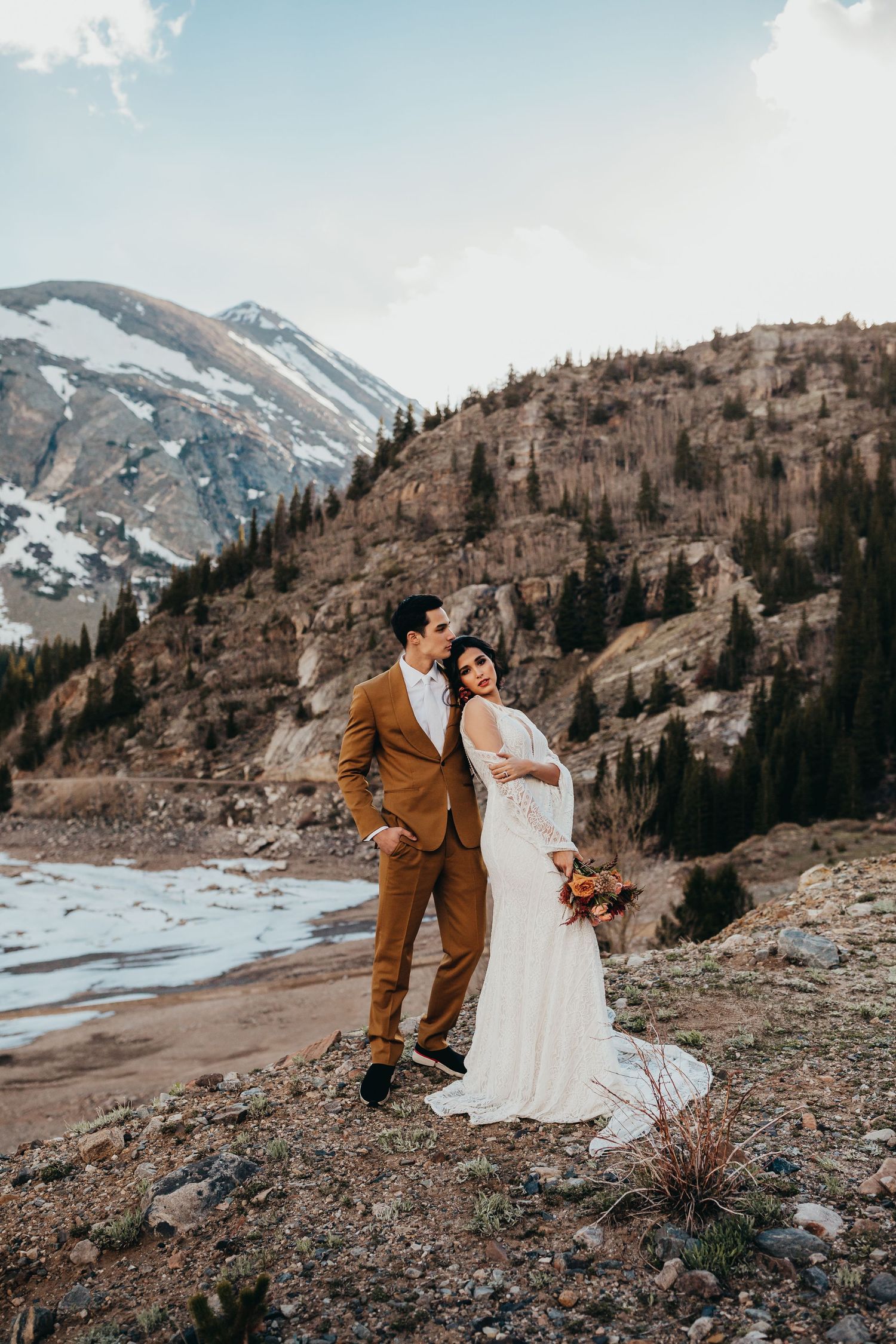 Elegant wedding portrait with couple standing against rugged mountain terrain and winter scenery.