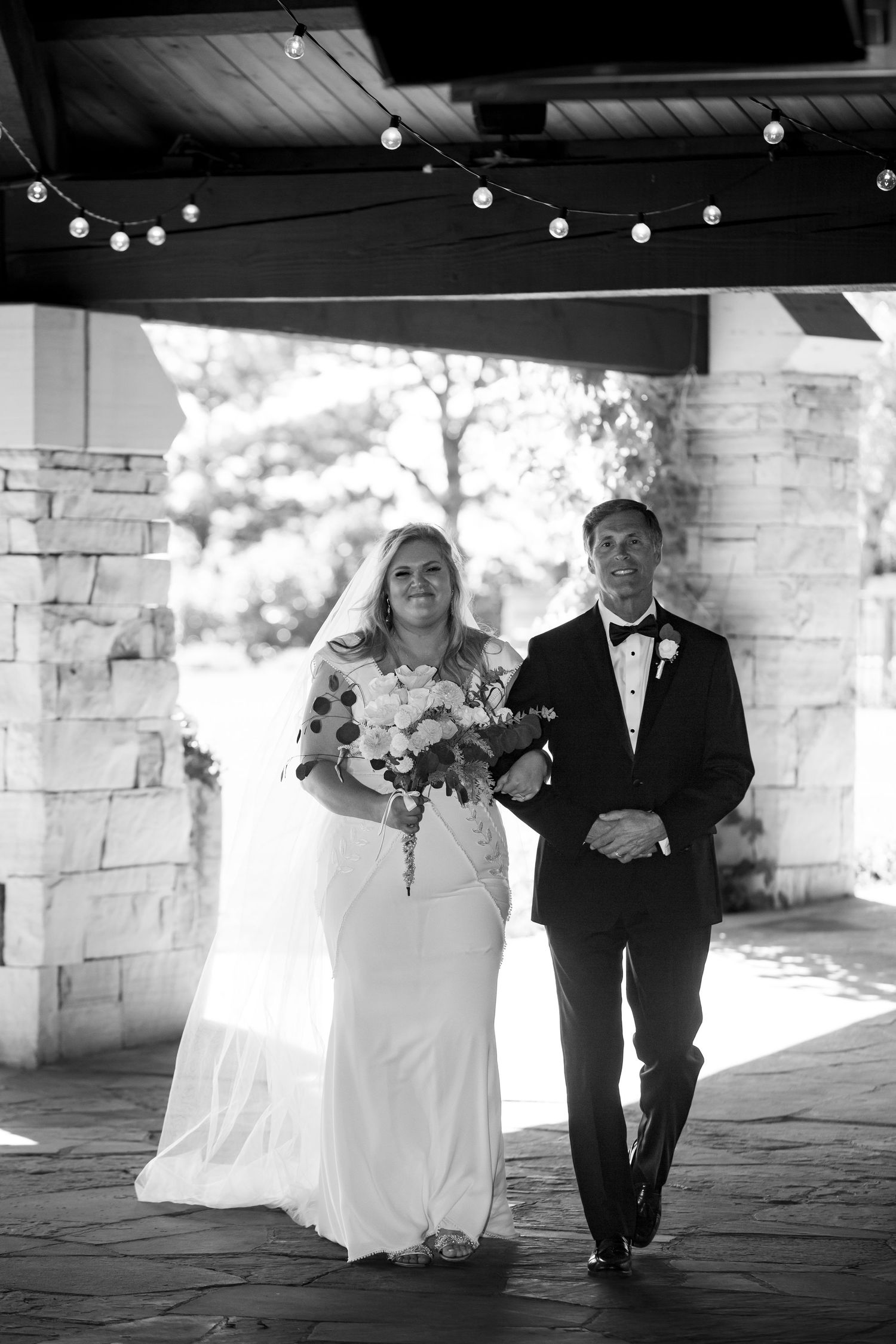 Wedding couple walking under string lights during formal ceremony.