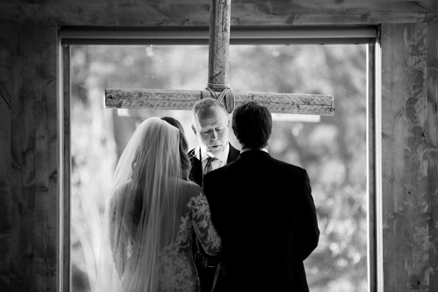 Black and white photo of wedding ceremony with couple and officiant framed in window.