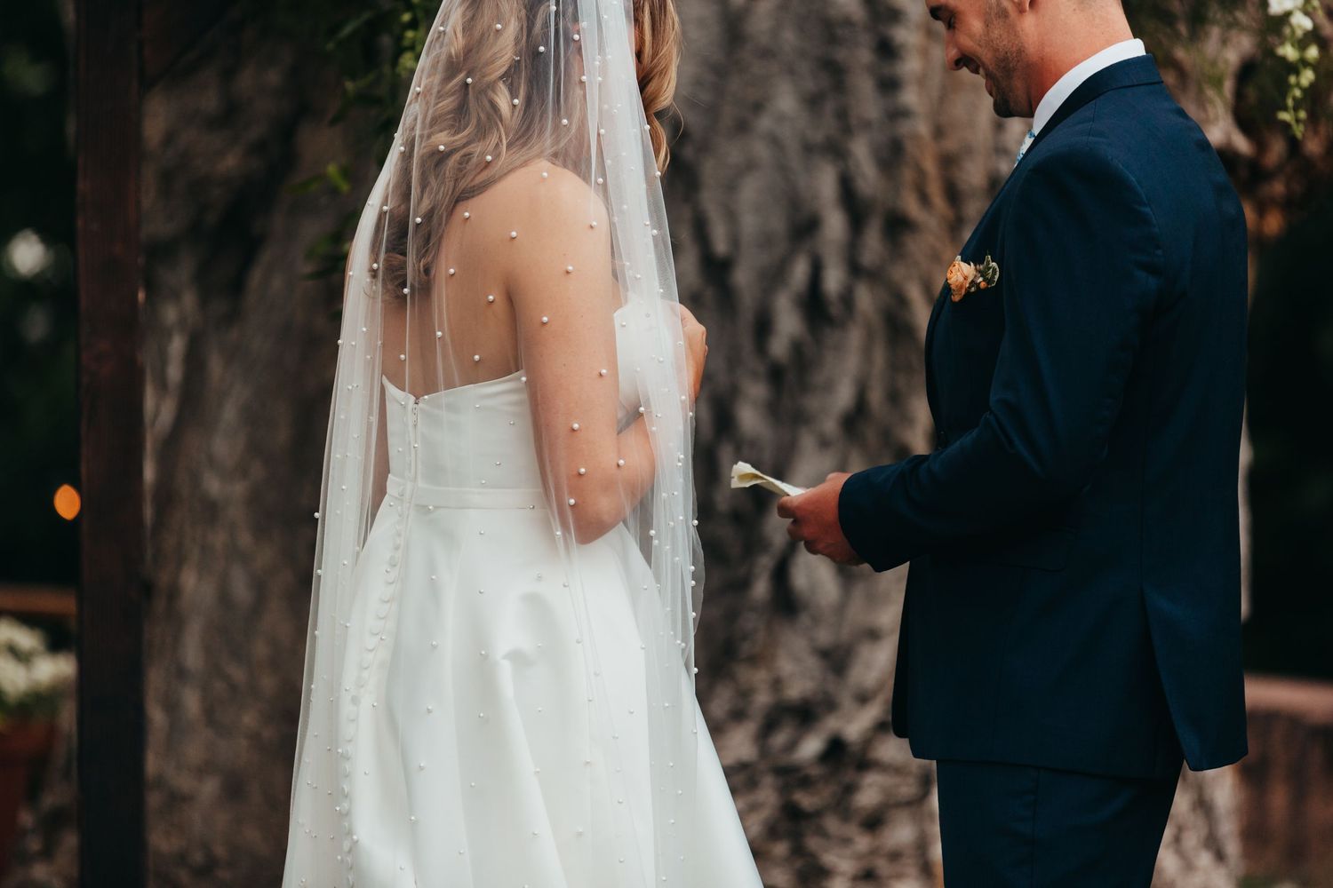 Wedding ceremony moment with couple exchanging vows beneath tall trees.