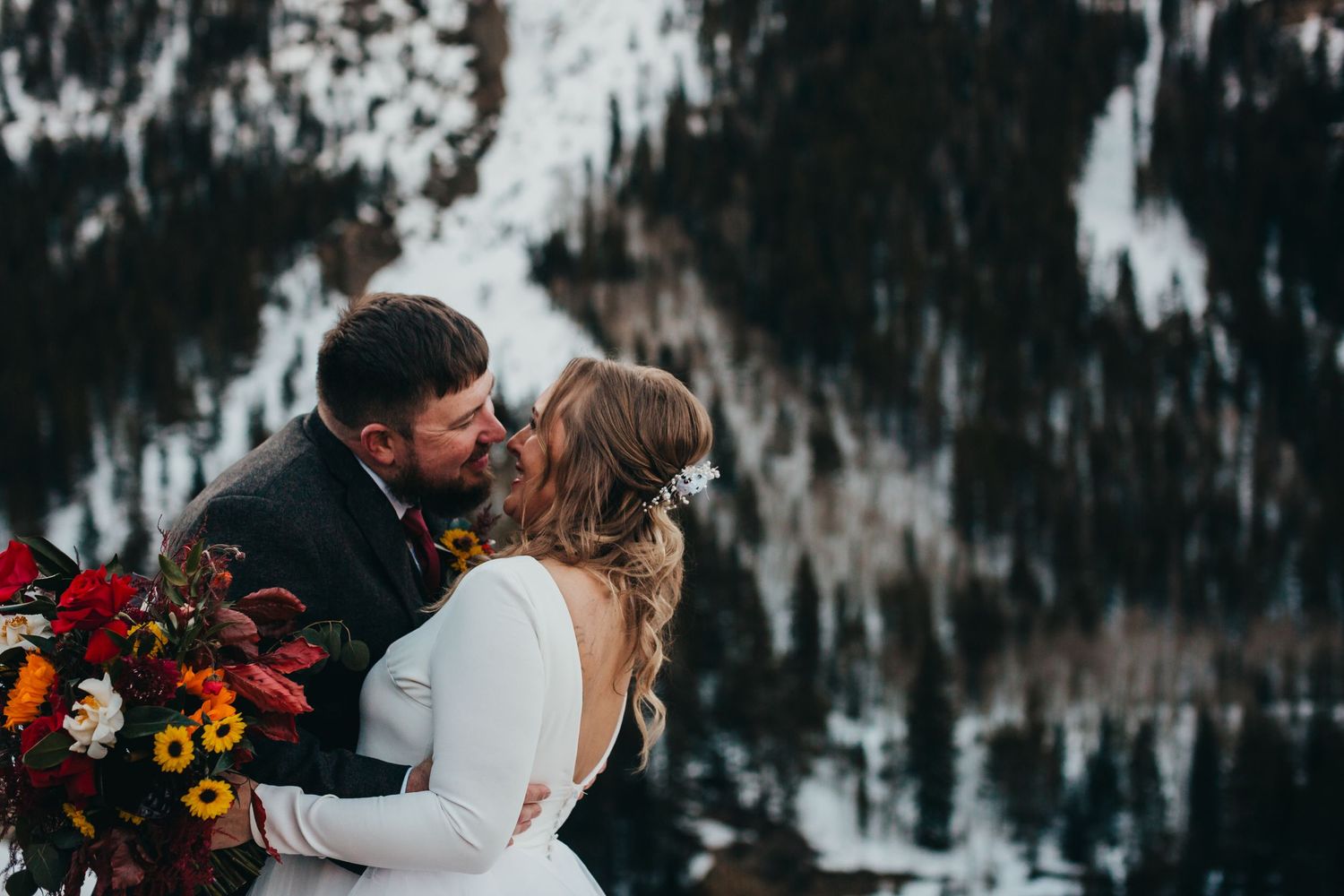 Newlyweds embrace in a winter mountain landscape with a vibrant wildflower bouquet.