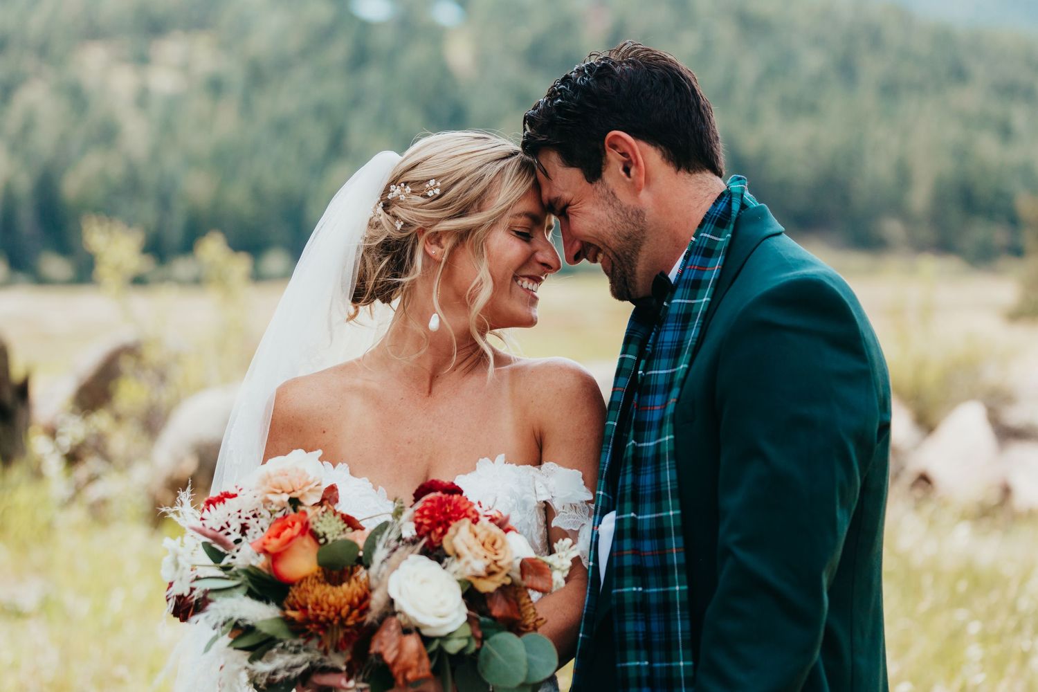 Intimate outdoor wedding moment with colorful autumn bouquet against mountain backdrop.