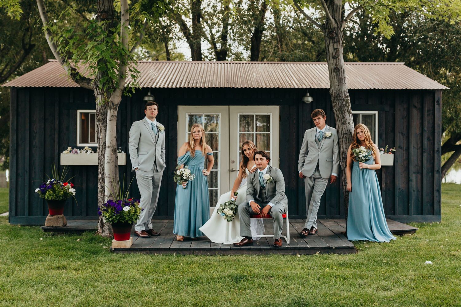 Wedding party poses on porch of black rustic cabin with bridesmaids in light blue dresses.