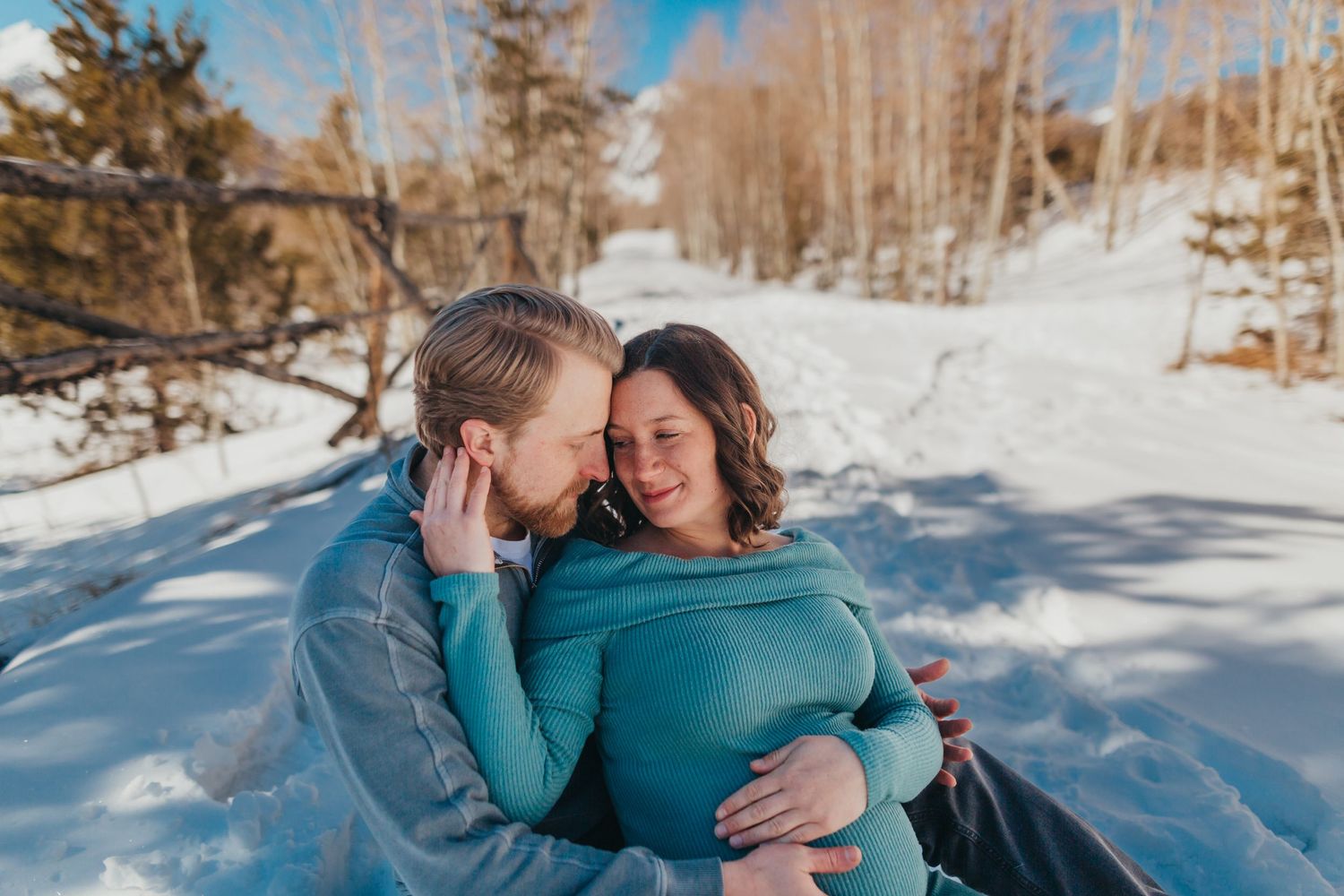 Couple shares intimate moment while sitting in snowy winter landscape.