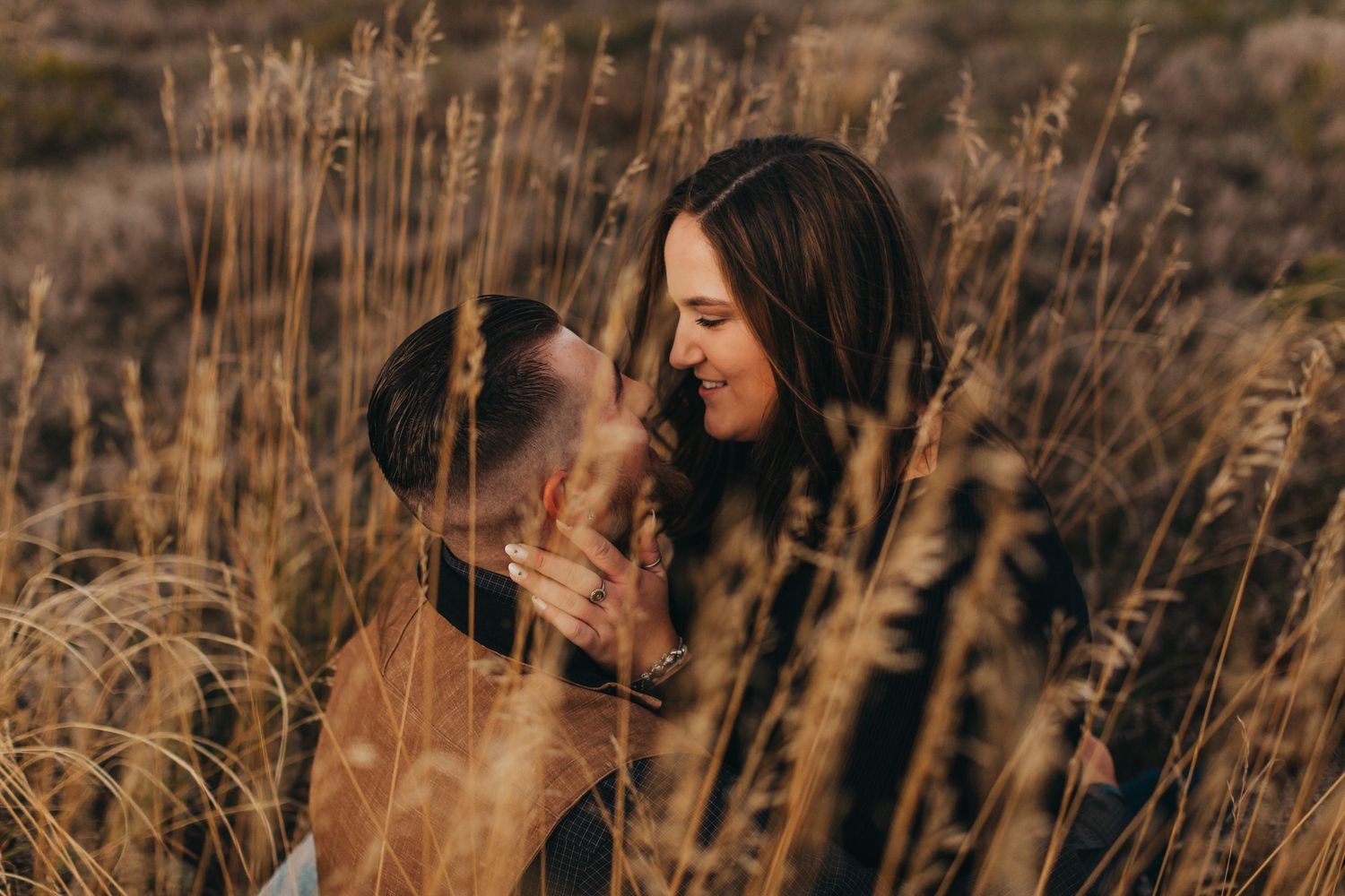 A person and dog share an intimate moment in tall golden grass during sunset.