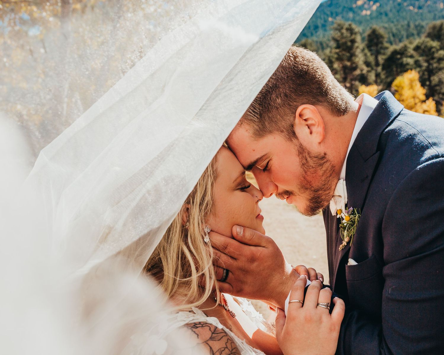 Intimate moment between newlyweds under flowing white veil.