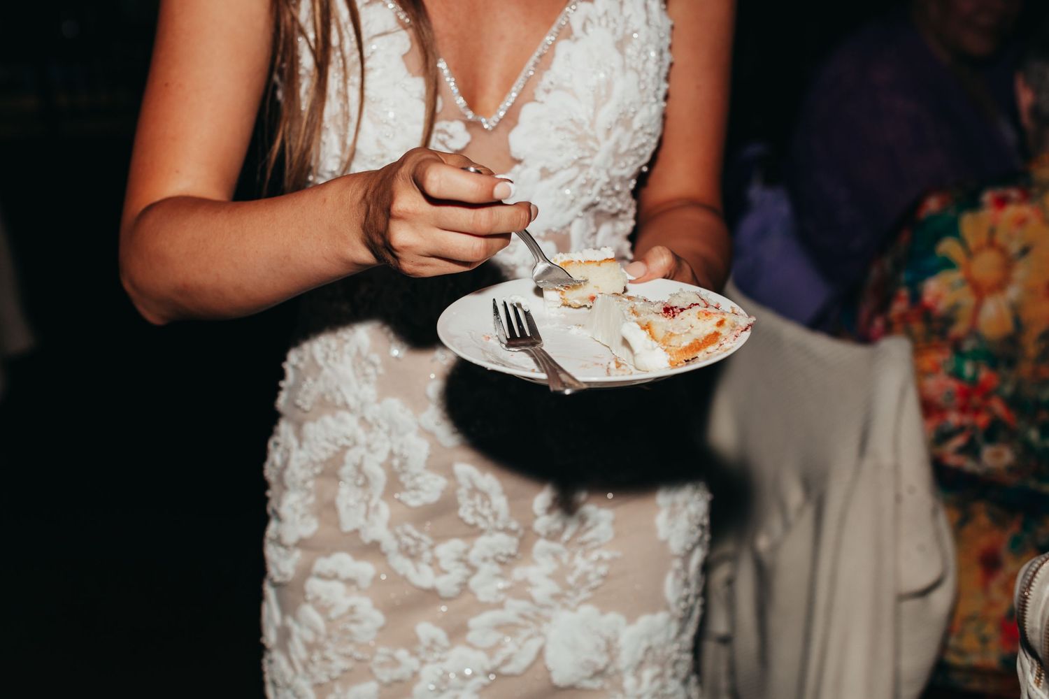 Close-up of white lace wedding dress detail while holding cake plate.