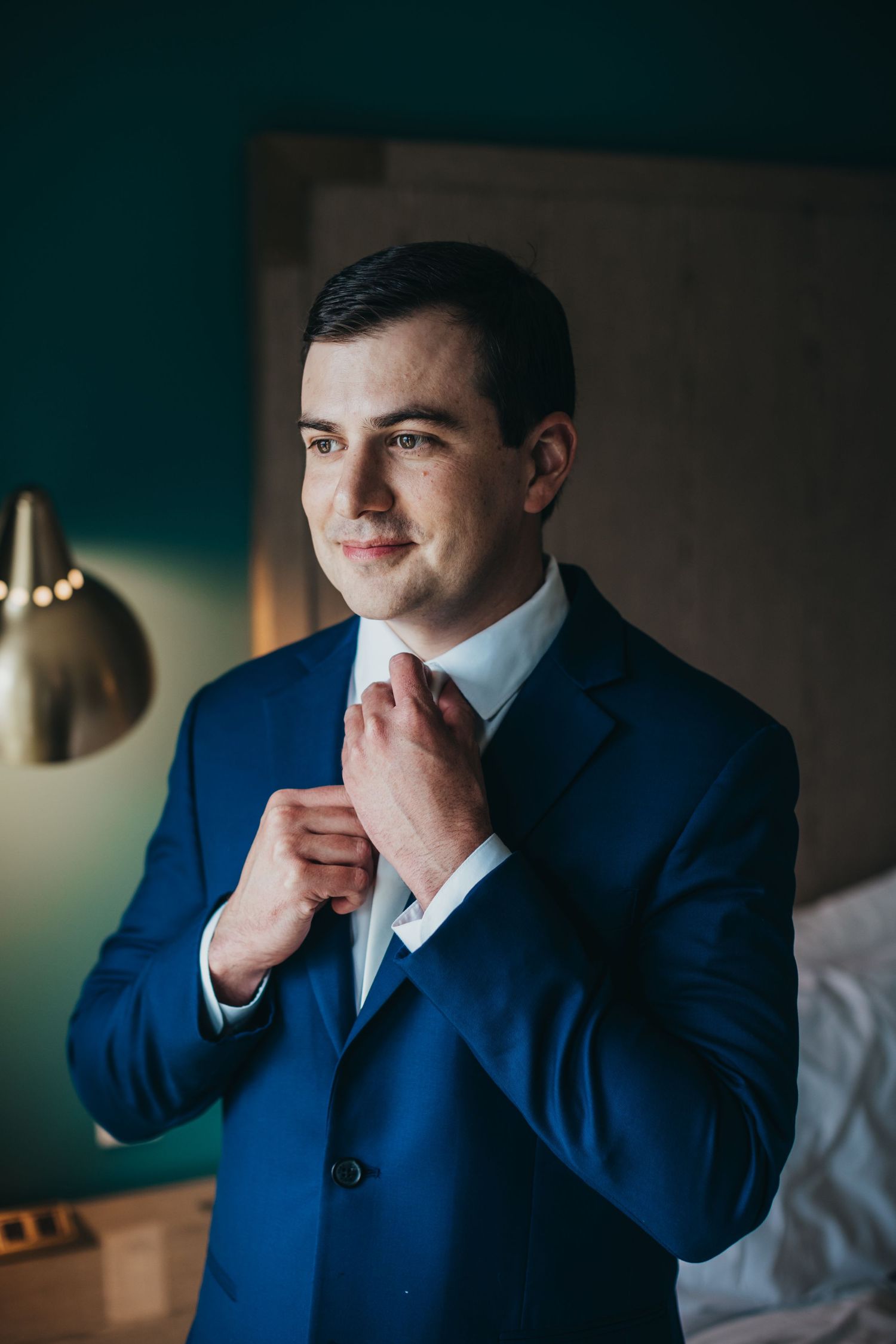 Groom adjusts tie while wearing navy blue suit before wedding ceremony.