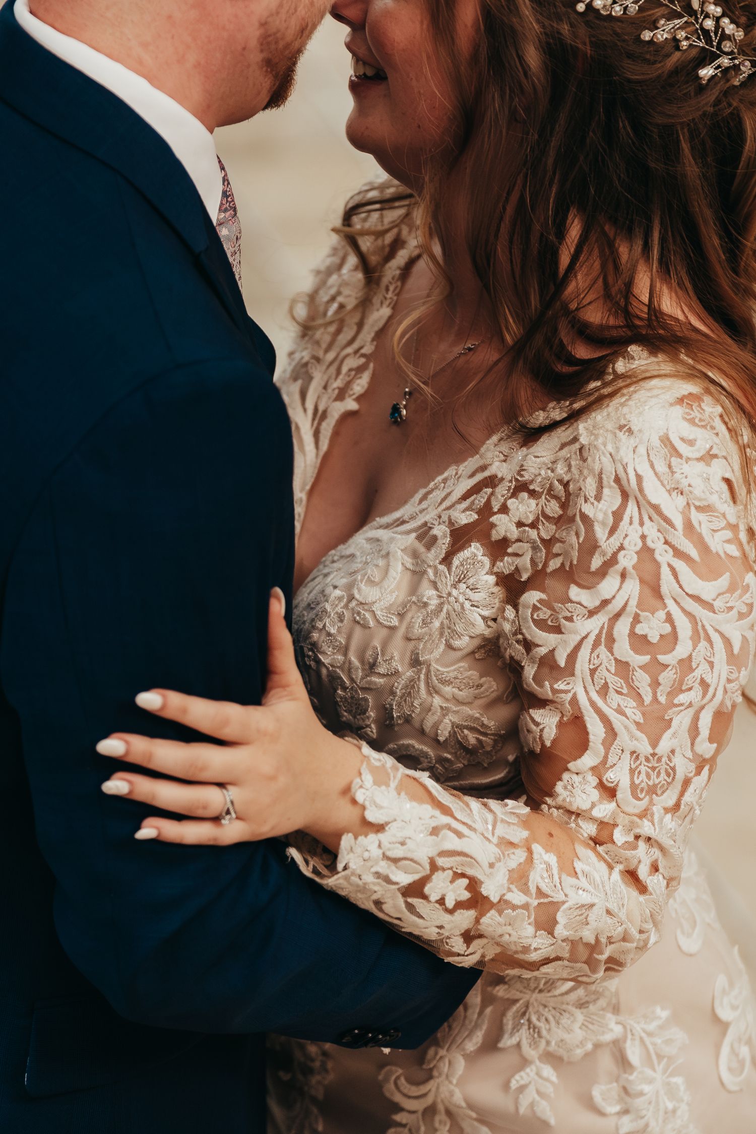 Close up of couple in wedding attire embracing showing intricate lace details.