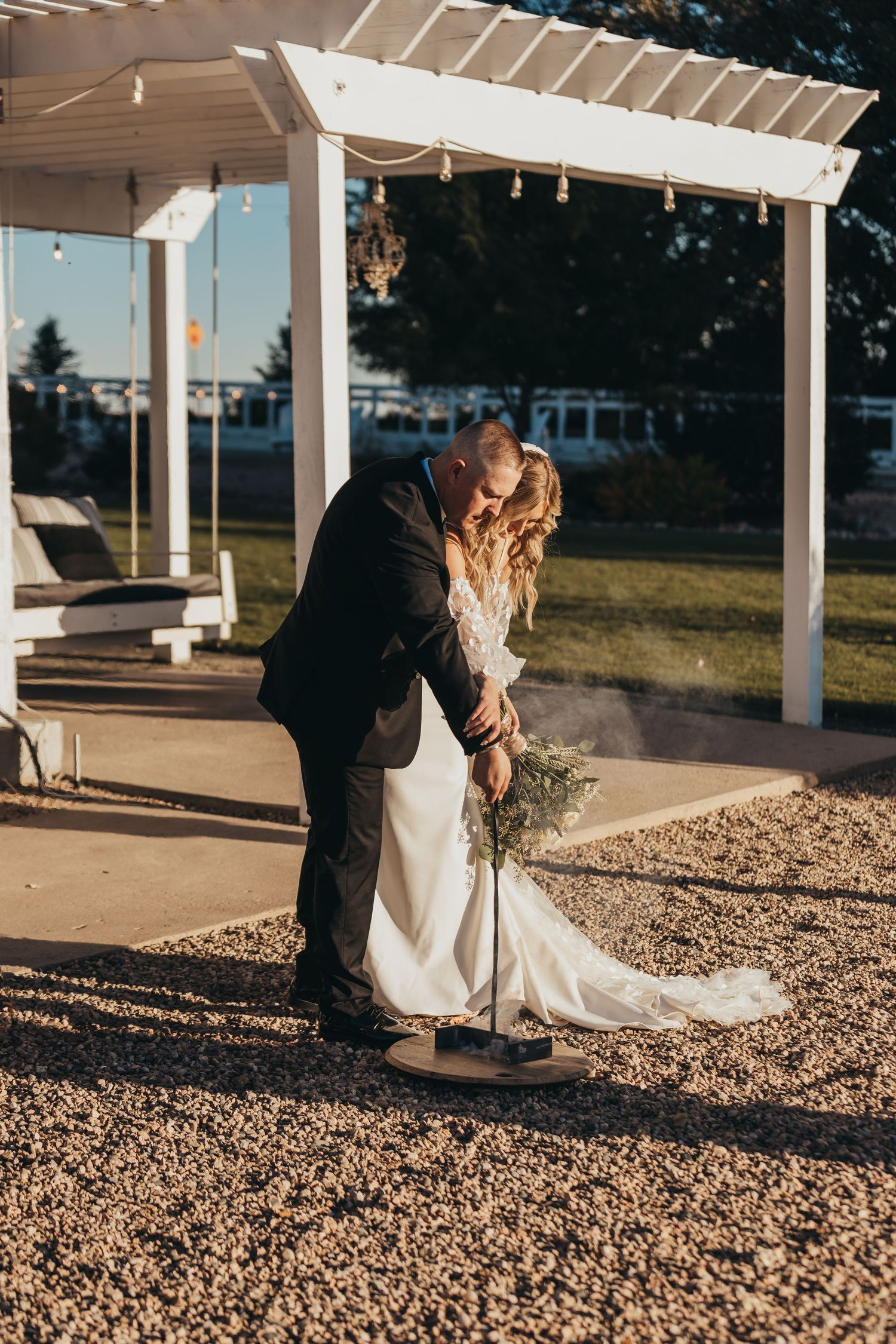 A romantic wedding moment under a white pergola during golden hour.