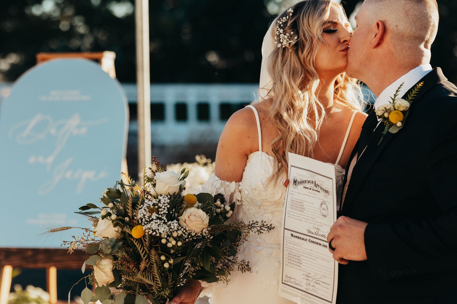 Romantic wedding moment with decorative sign and floral arrangements in outdoor setting.
