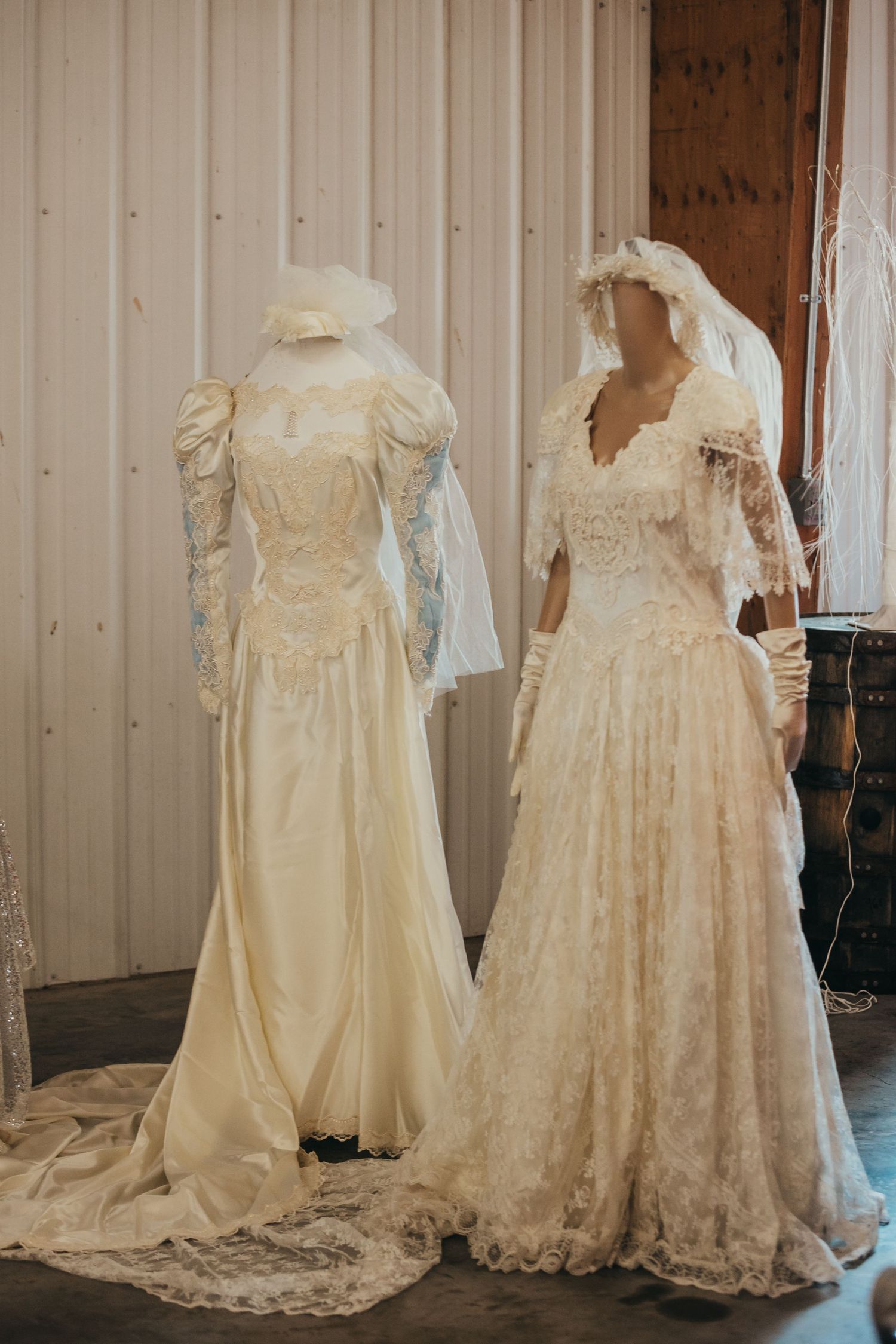 Two vintage-style wedding dresses on display with intricate lace and flowing trains.