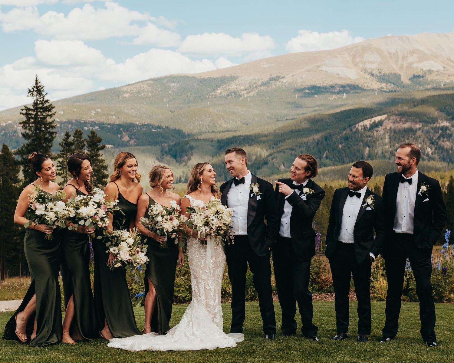 Wedding party poses together against scenic mountain backdrop with vibrant blue skies.