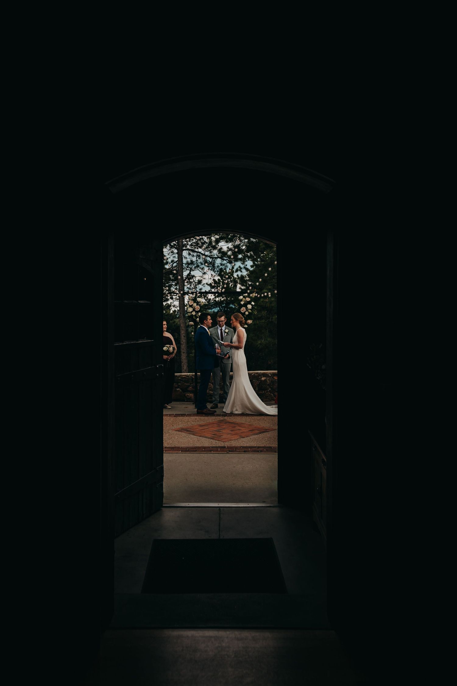 Wedding couple silhouette framed through dark doorway with natural light streaming in.