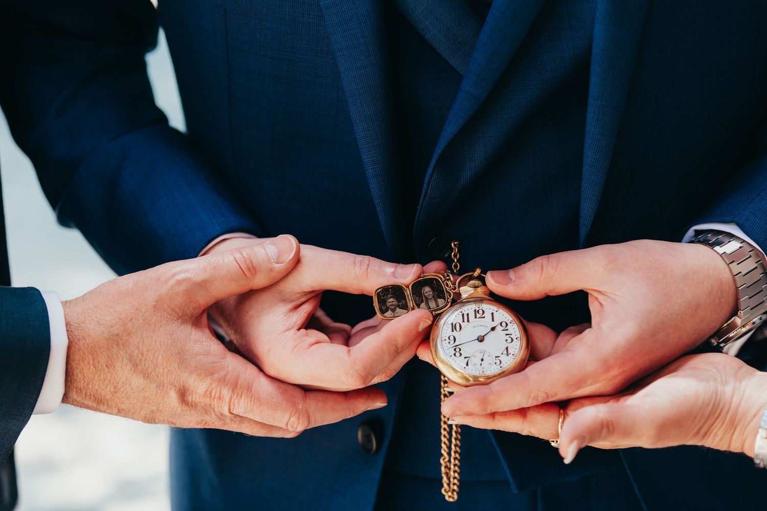 Hands holding an antique pocket watch against a navy blue suit jacket.