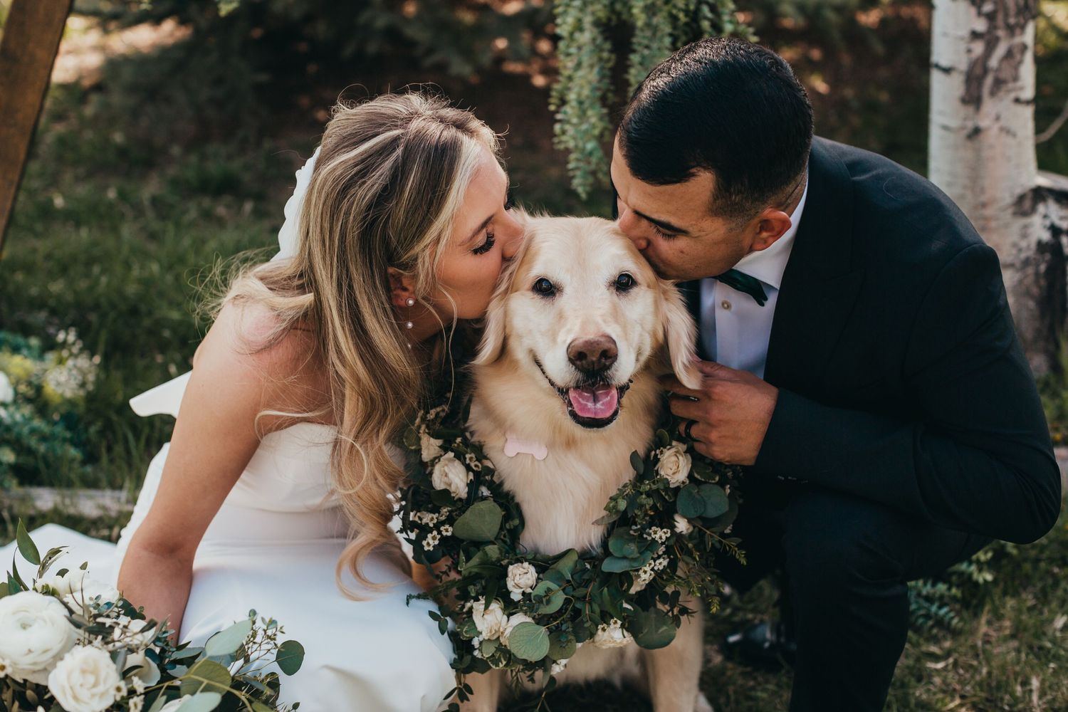 Happy couple sharing a moment with their golden retriever wearing a floral collar at their wedding.