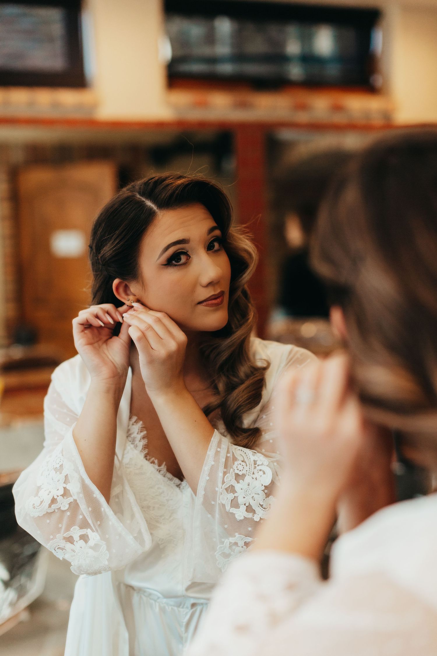 Bride getting ready with makeup and delicate lace robe in warm lighting.