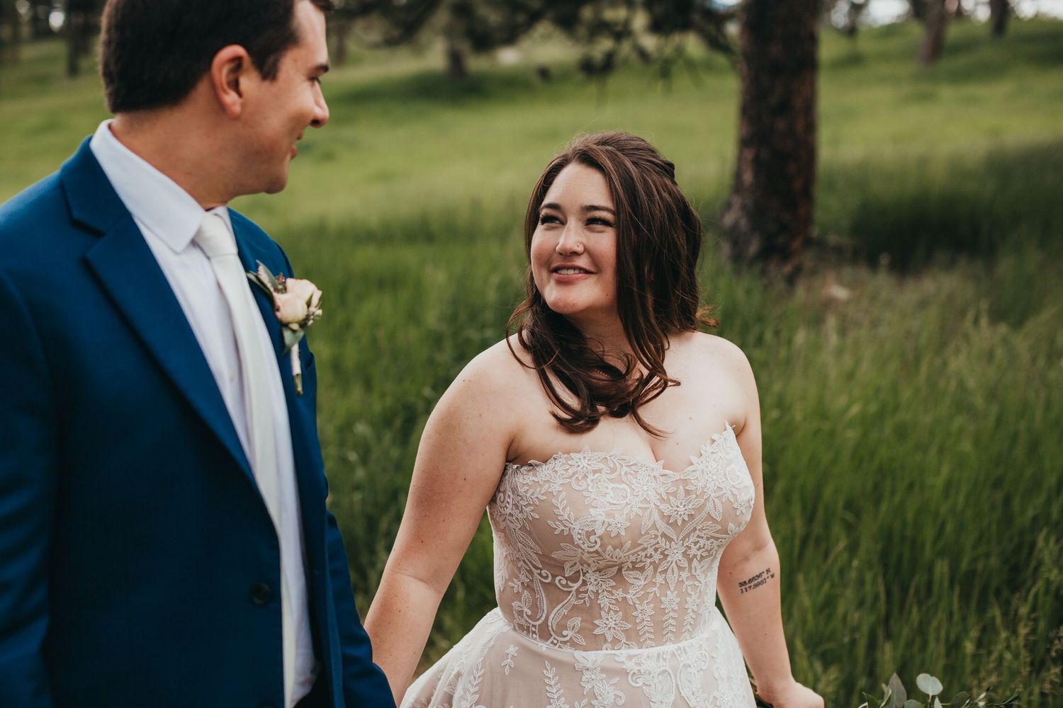 Wedding couple in blue suit and lace dress standing in a grassy mountain meadow.