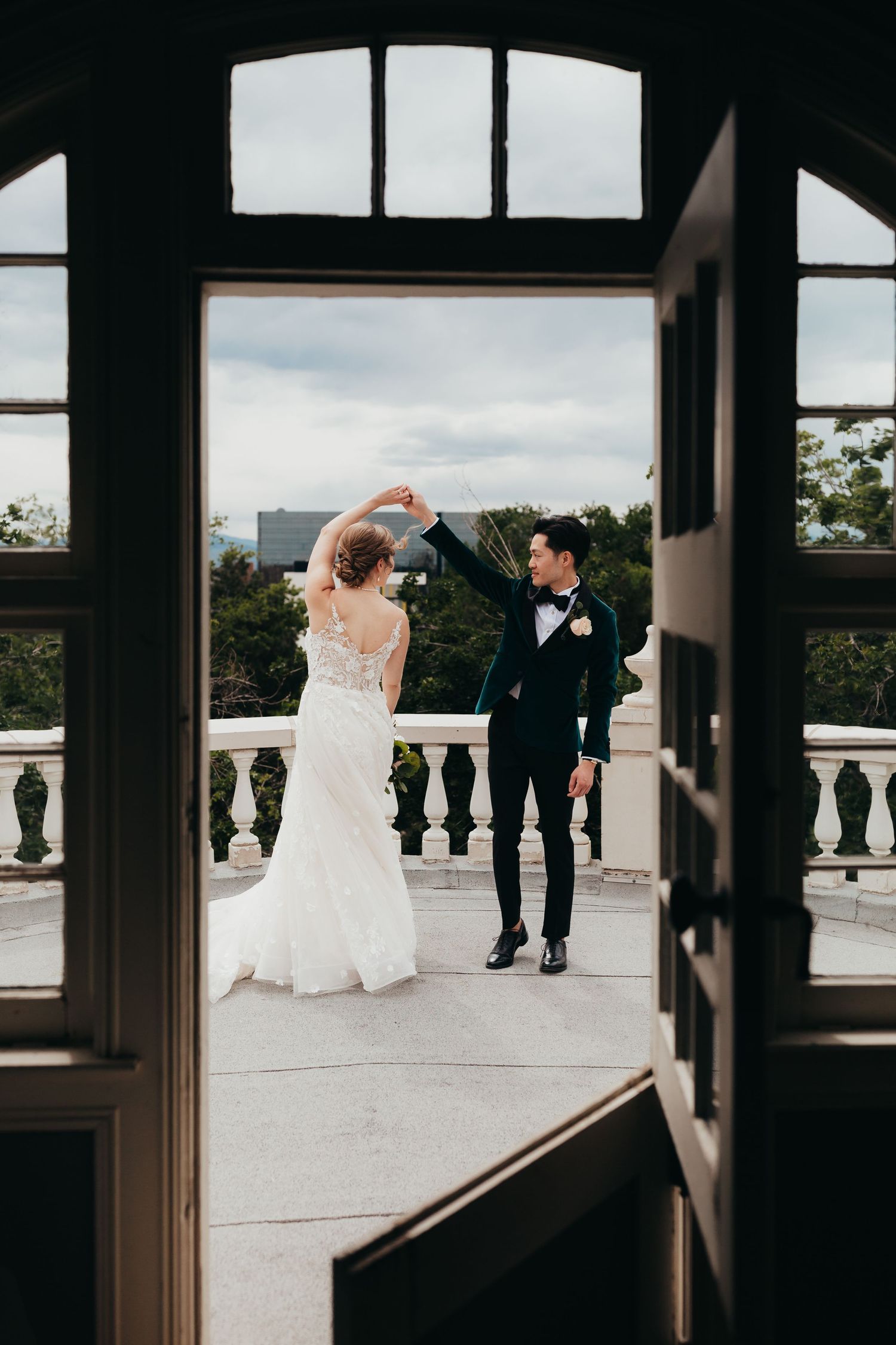 A couple shares a dance moment on an elegant balcony framed by architectural doorways.