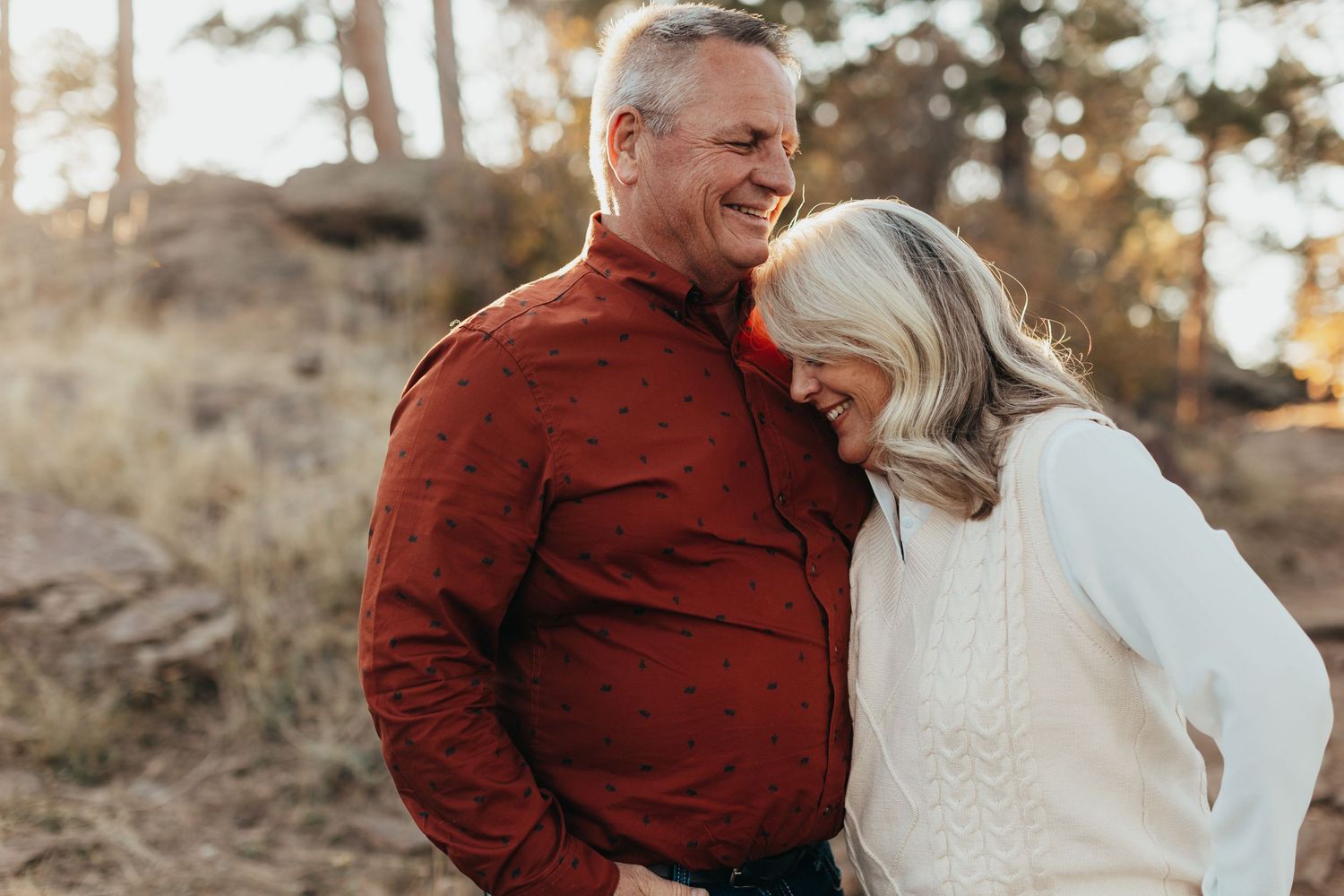 Mature couple embraces during sunset photoshoot in natural outdoor setting.