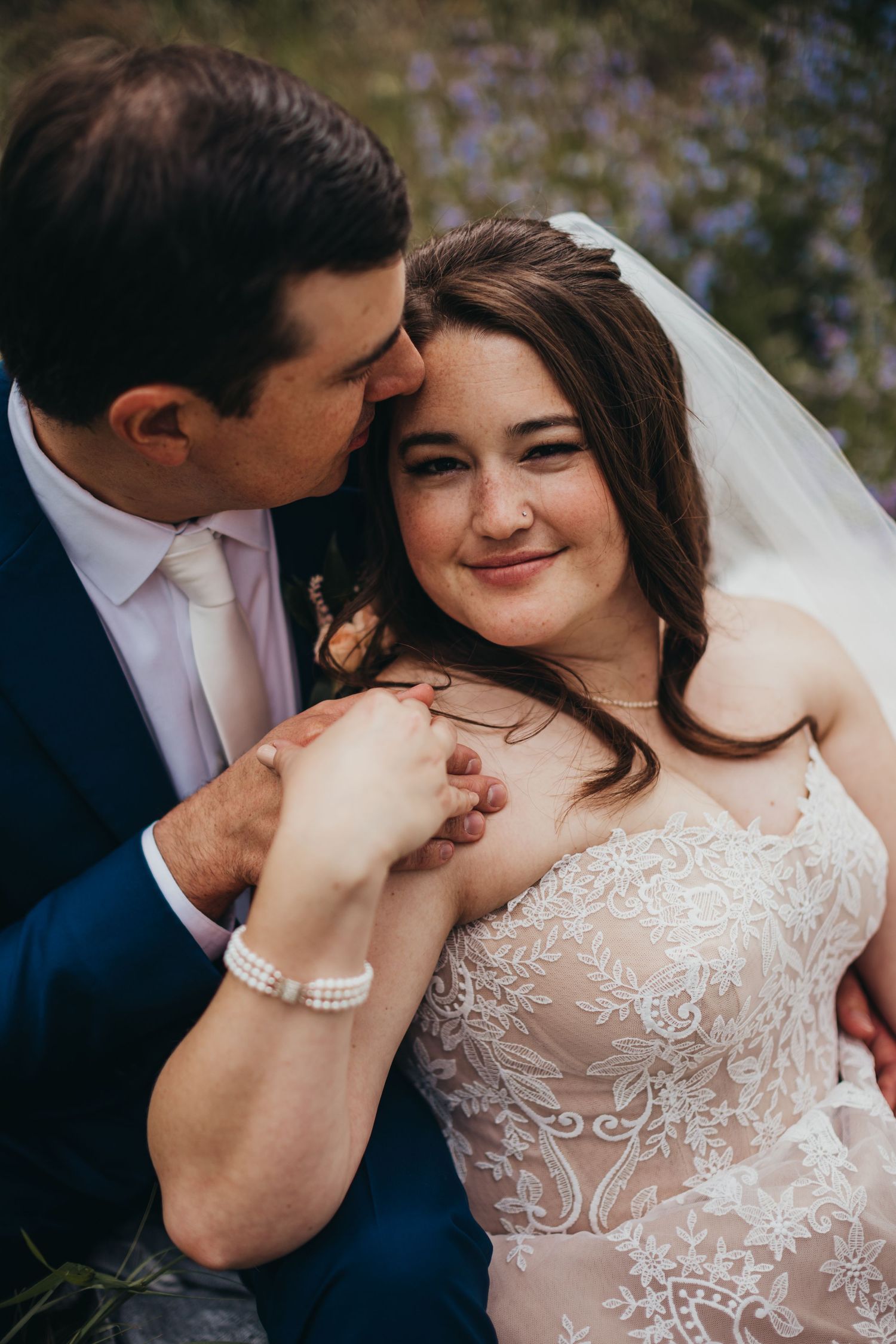 Romantic wedding portrait with couple sharing tender moment among purple wildflowers.