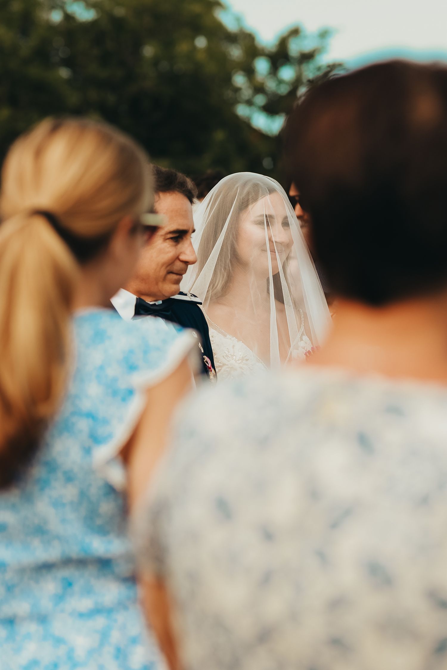 A tender moment during a wedding ceremony with guests in blue dresses and formal attire looking on.