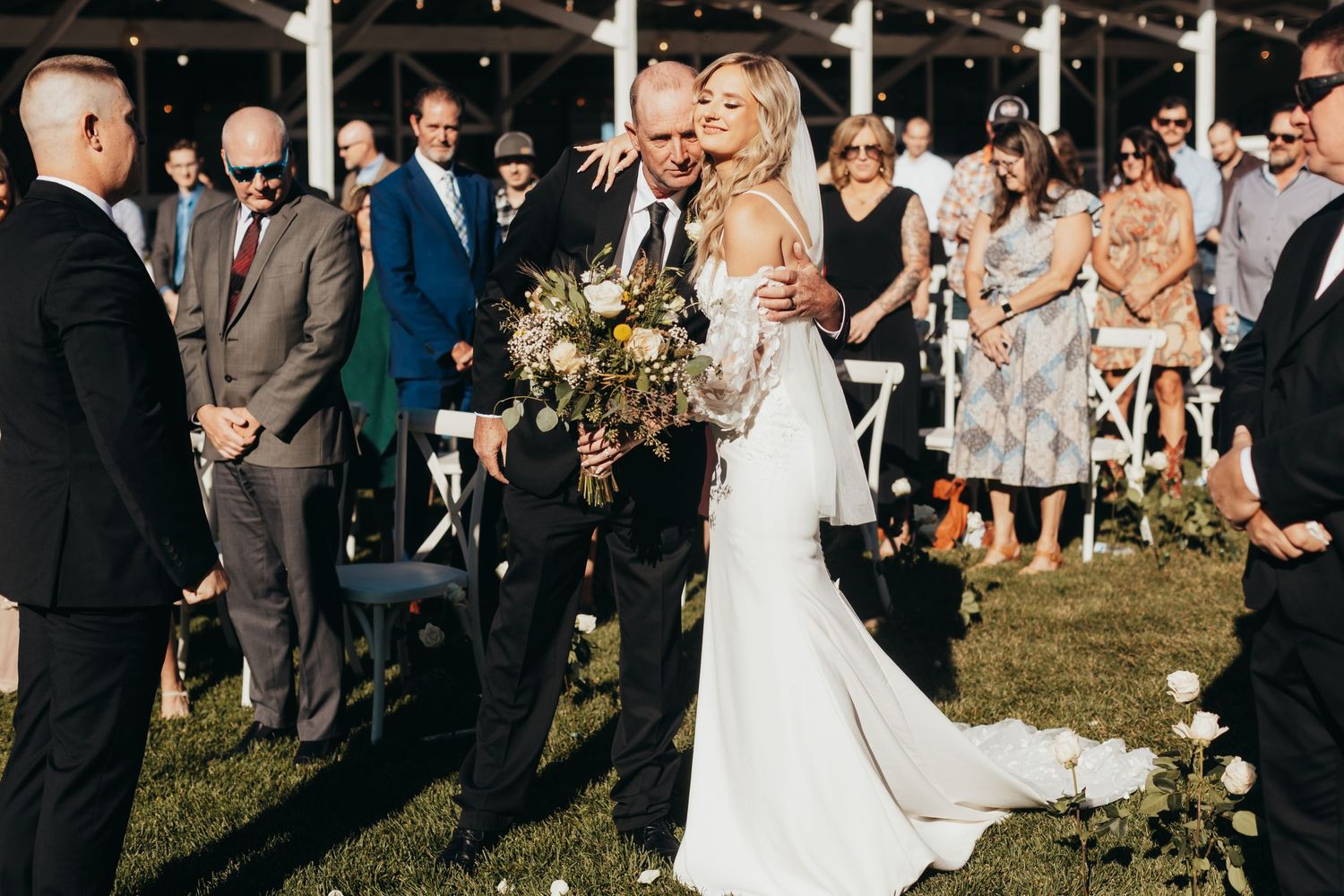 Outdoor wedding ceremony with guests watching couple exchange vows under clear skies.