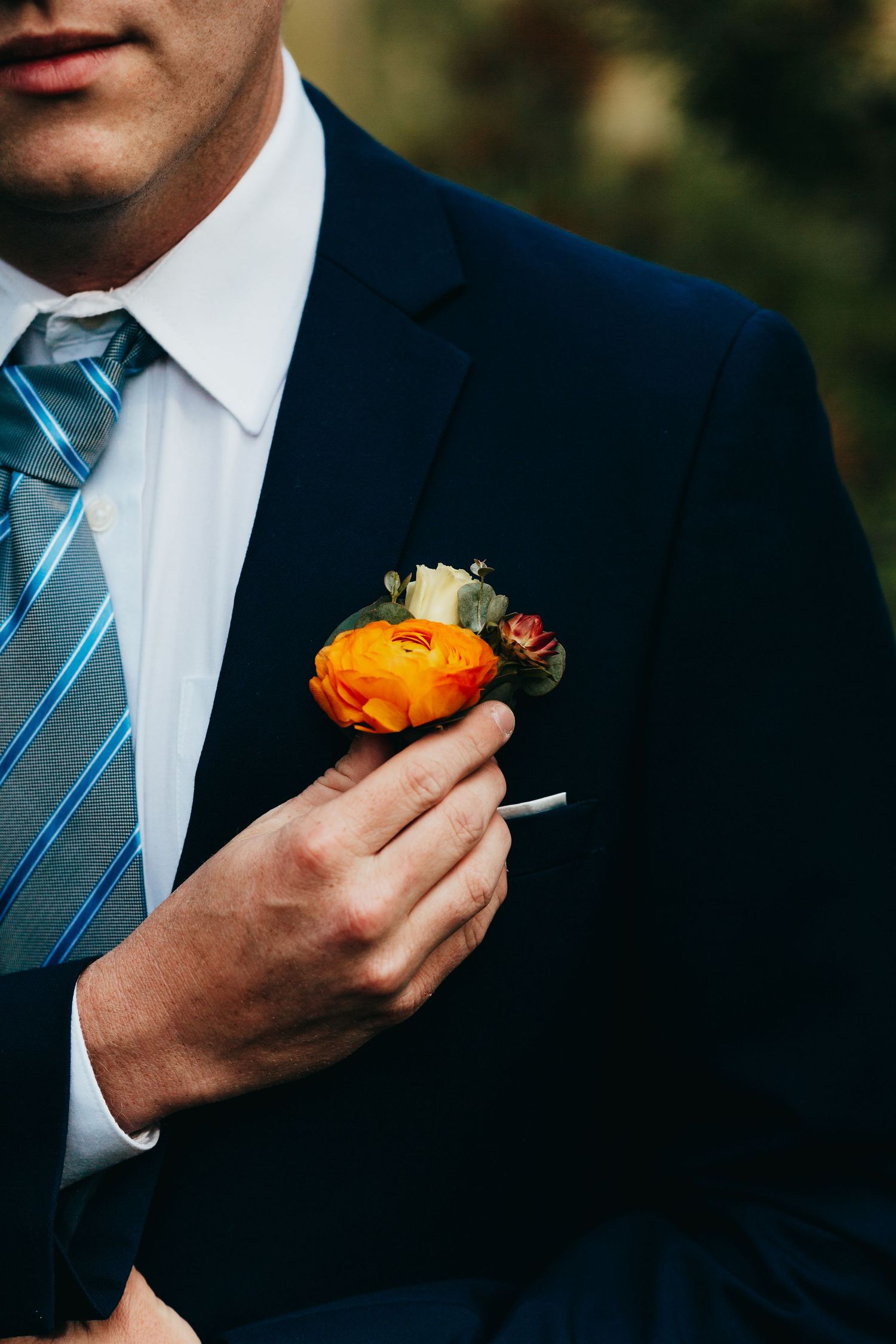 Close-up of orange boutonniere on navy suit with striped tie.