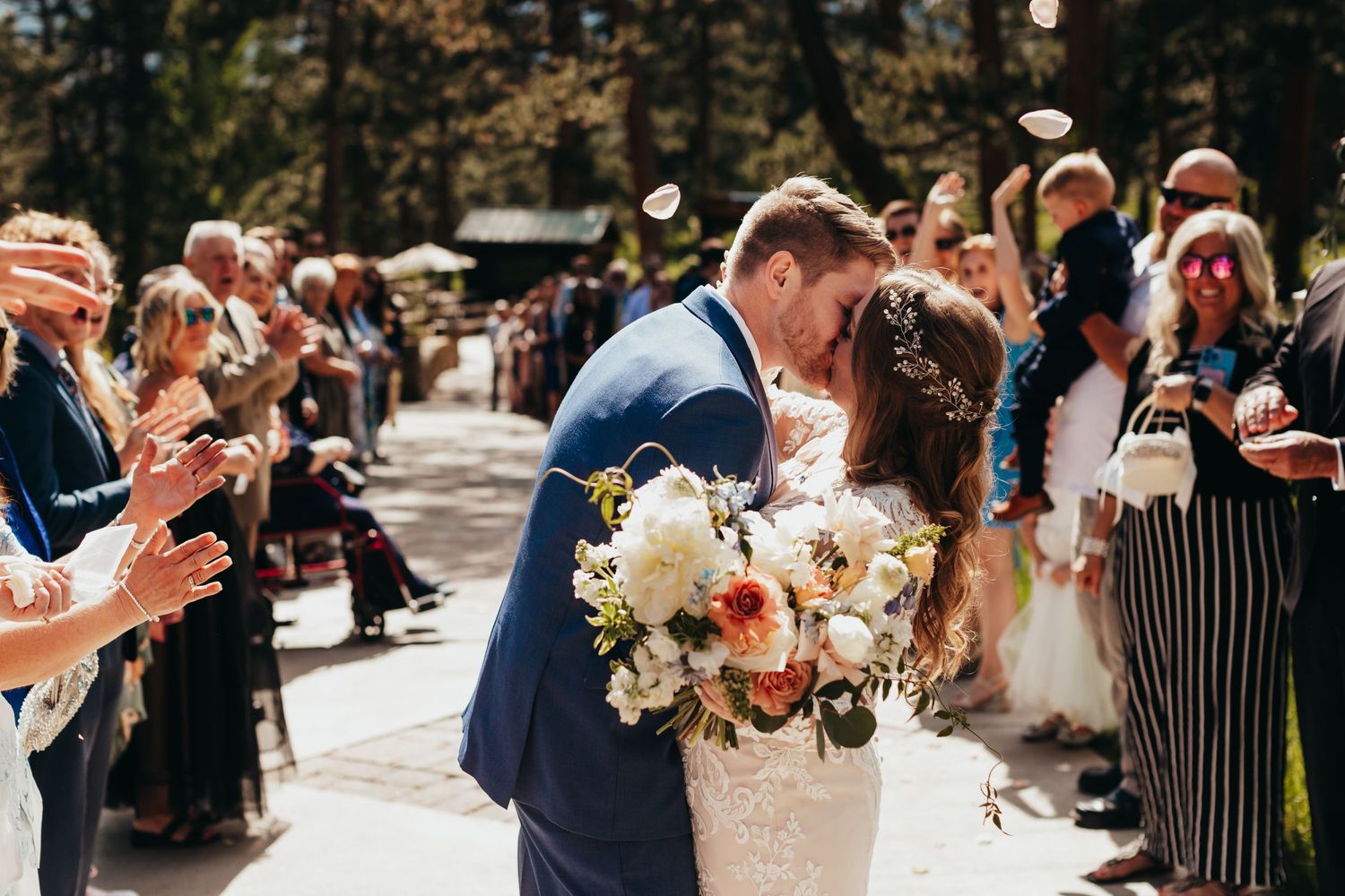 Wedding ceremony guests celebrate as a couple shares their first kiss on a sunny outdoor patio.