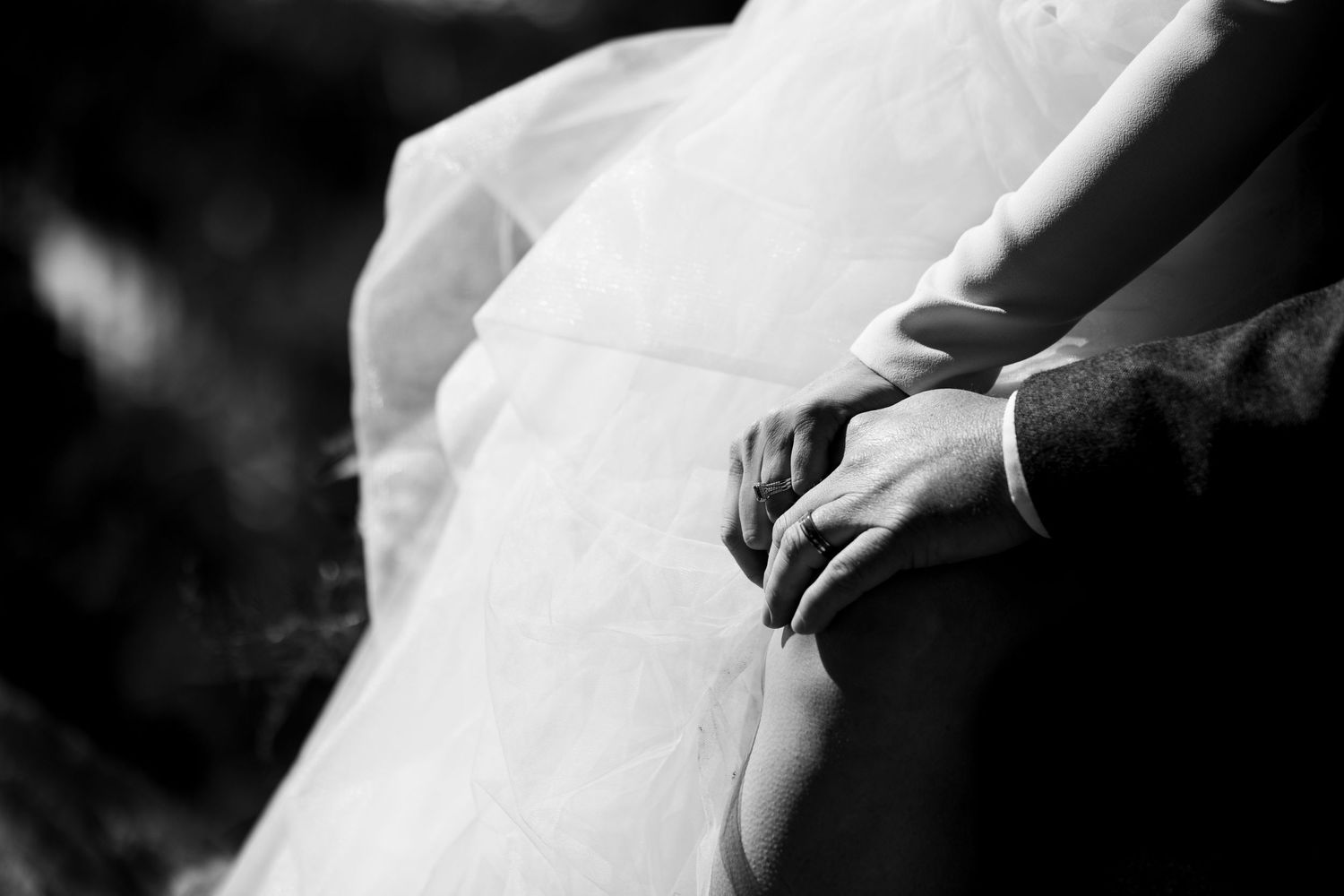 A black and white detail shot of hands resting on wedding dress fabric.
