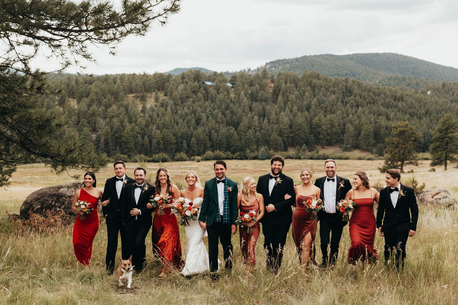 Wedding party in red and black attire walks together across a scenic mountain landscape.