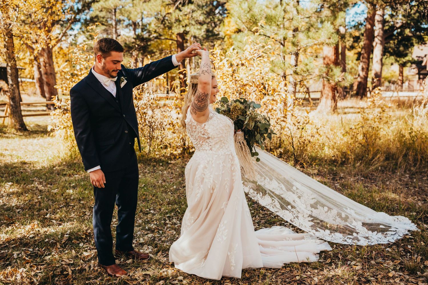 Couple in formal wedding attire posing among golden autumn trees in a forest setting.