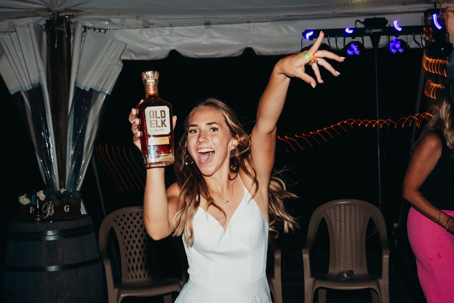 A festive wedding reception celebration under a tent with string lights and lively dancing.