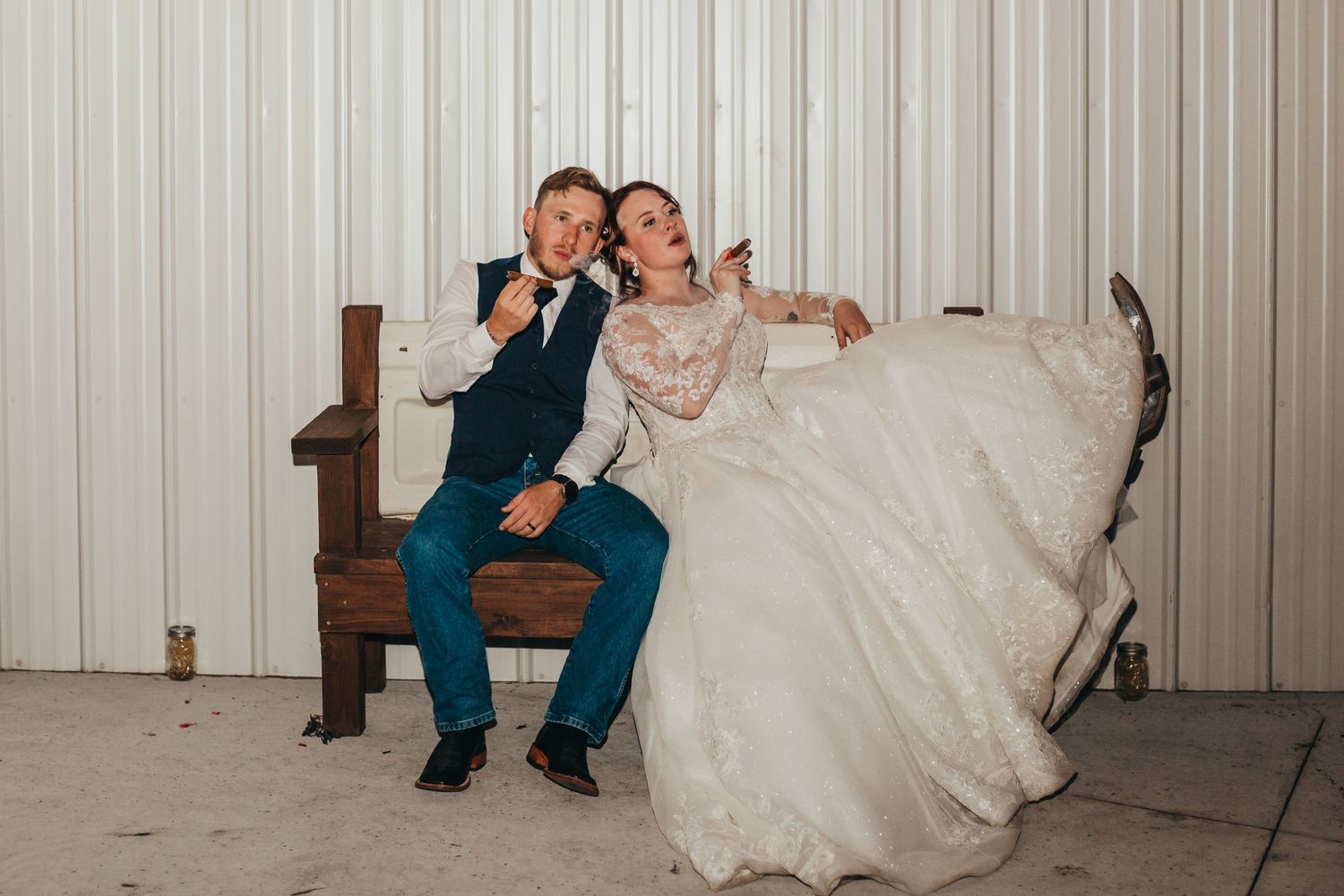 Playful couple poses on vintage bench at wedding reception venue.