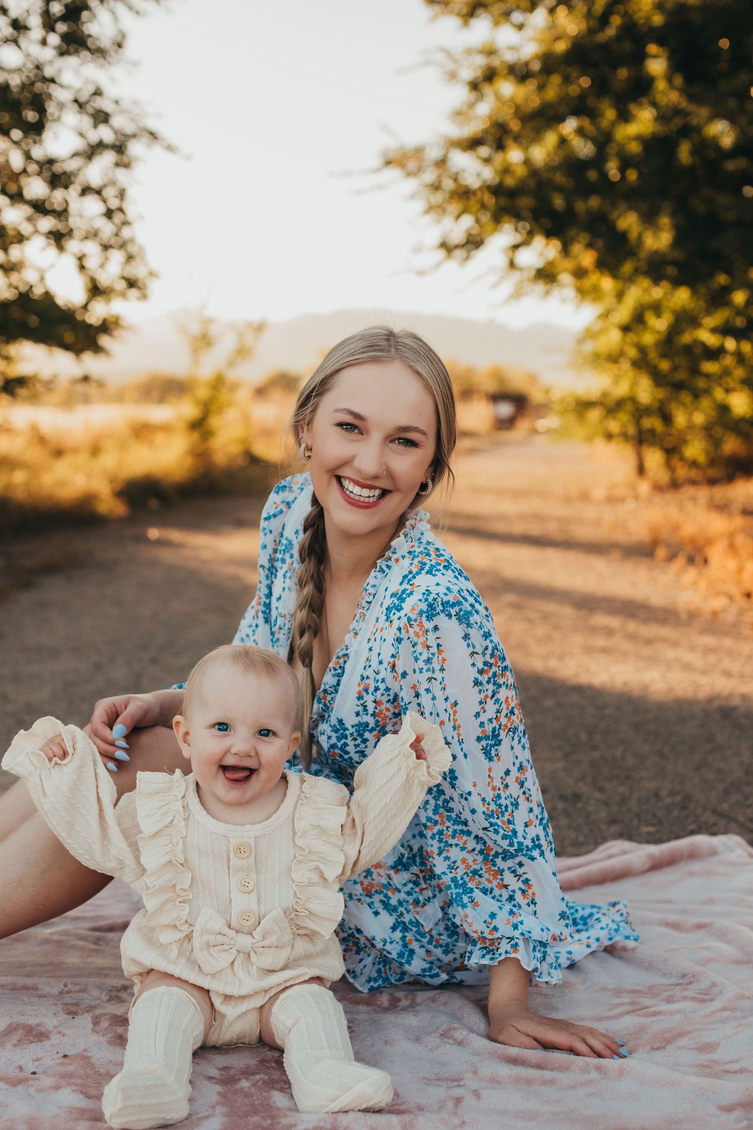 Mother and baby in matching light tones sit on blanket during golden hour photo session.