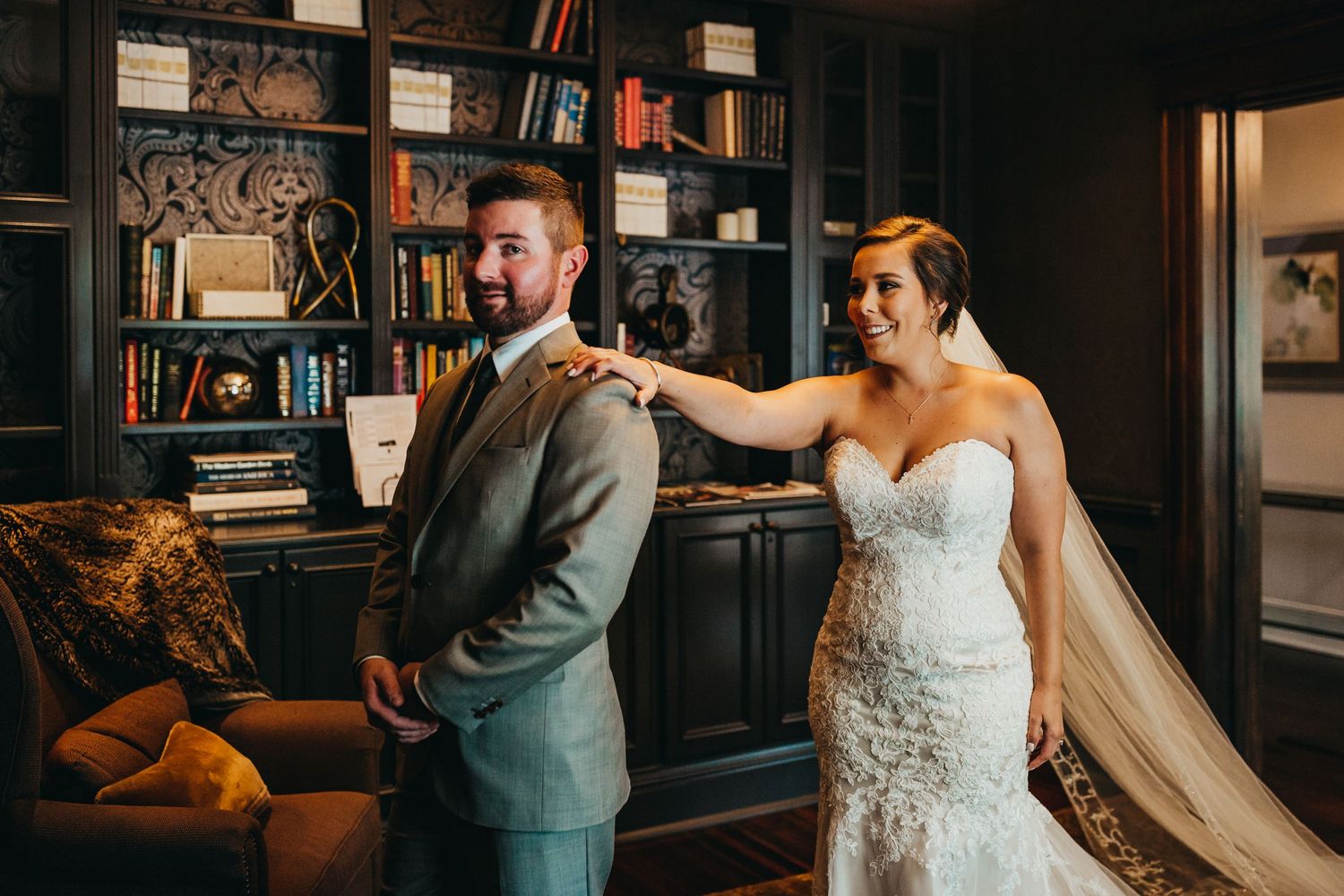 First look moment between couple in elegant library with built-in bookshelves.