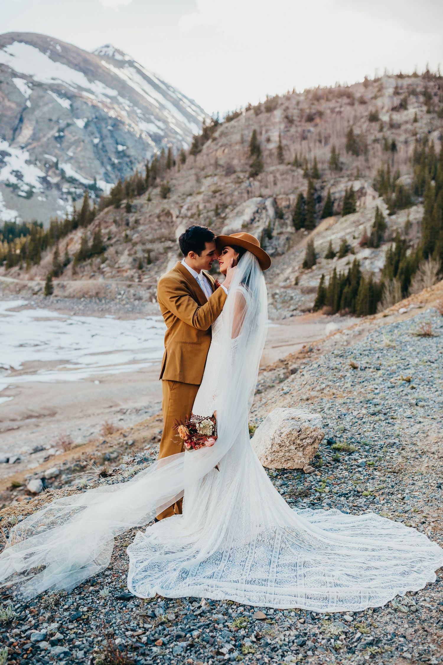 A dreamy winter wedding scene with a cathedral length veil against snow-dusted mountains.