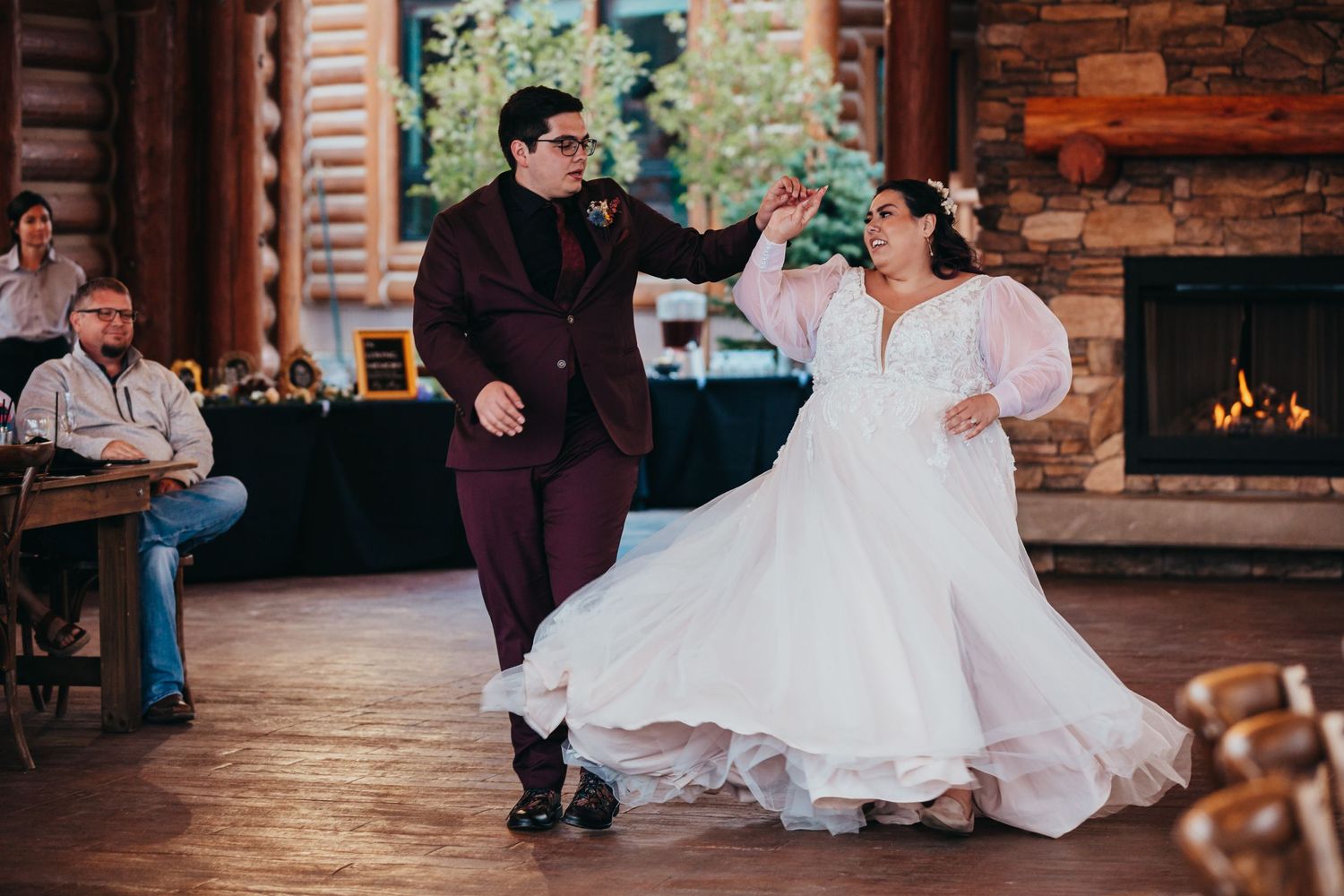 Couple dancing together at a rustic wedding reception venue with wooden beams and fireplace.