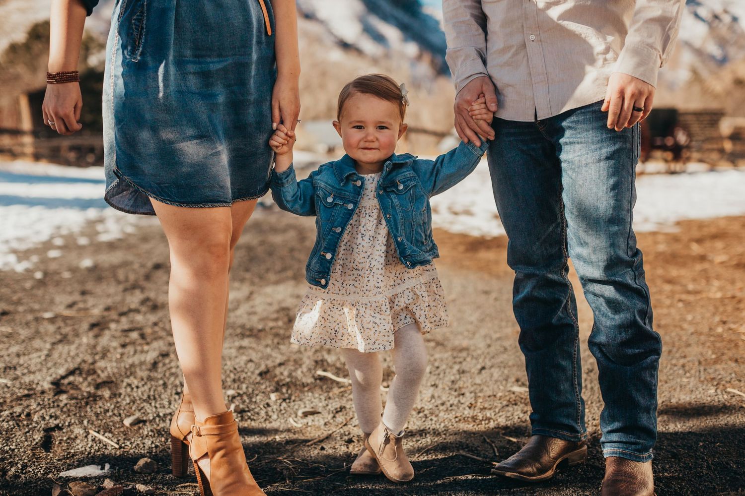 Child in denim jacket walking between parents on outdoor path.