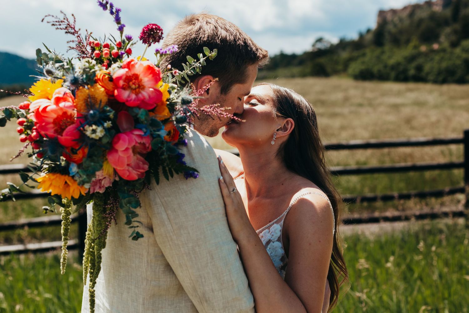 A vibrant wildflower bouquet with orange and red blooms complements a romantic outdoor wedding moment.
