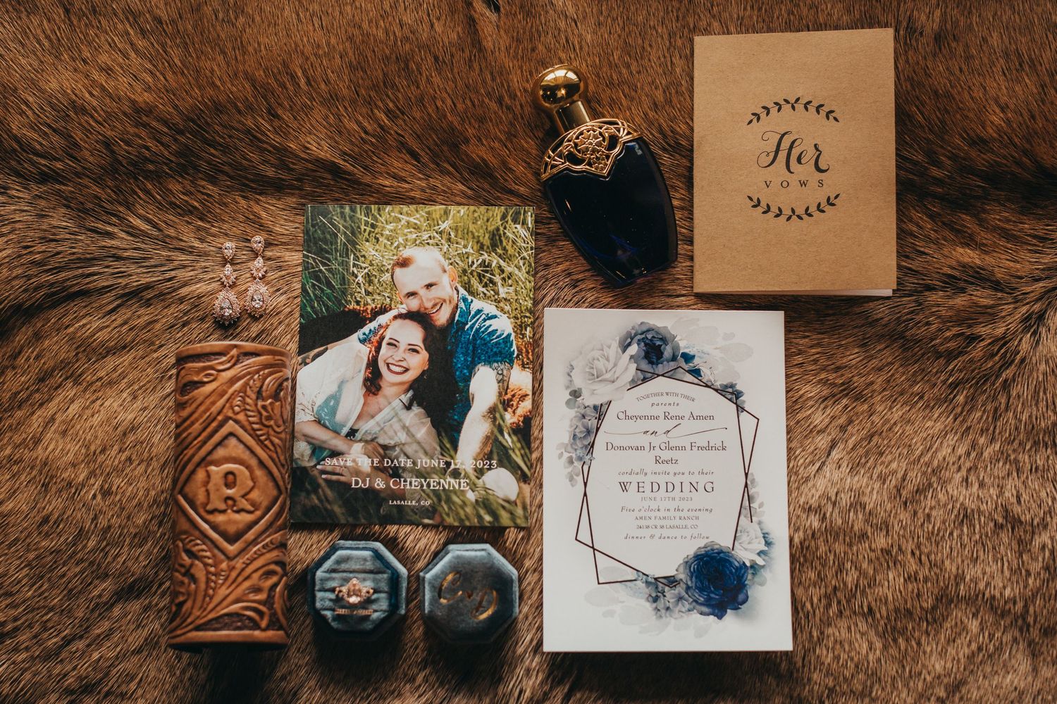 Wedding details flatlay with invitation, rings, and photo on brown leather background.