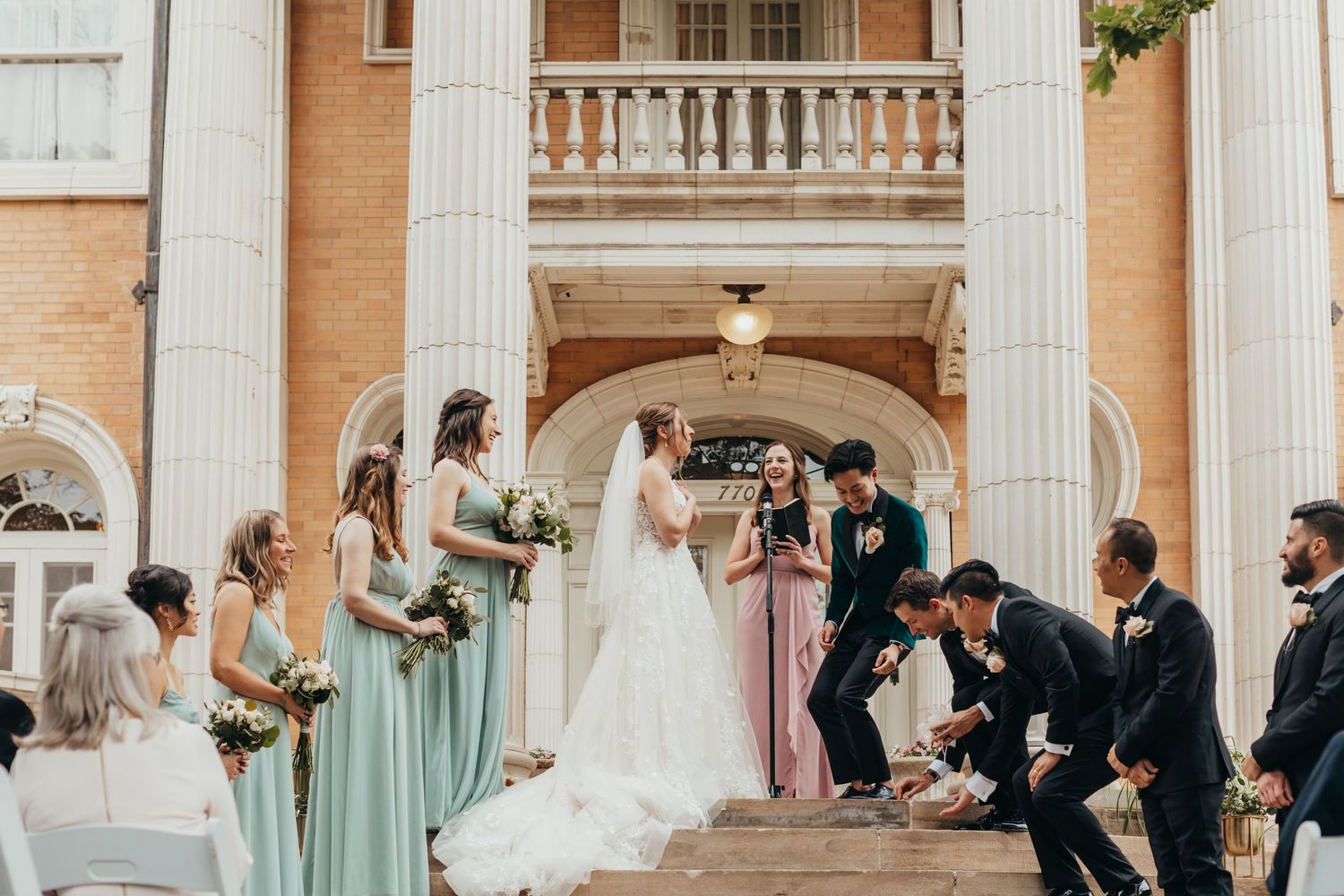 A wedding party poses on classical architecture steps with bridesmaids in mint green dresses.